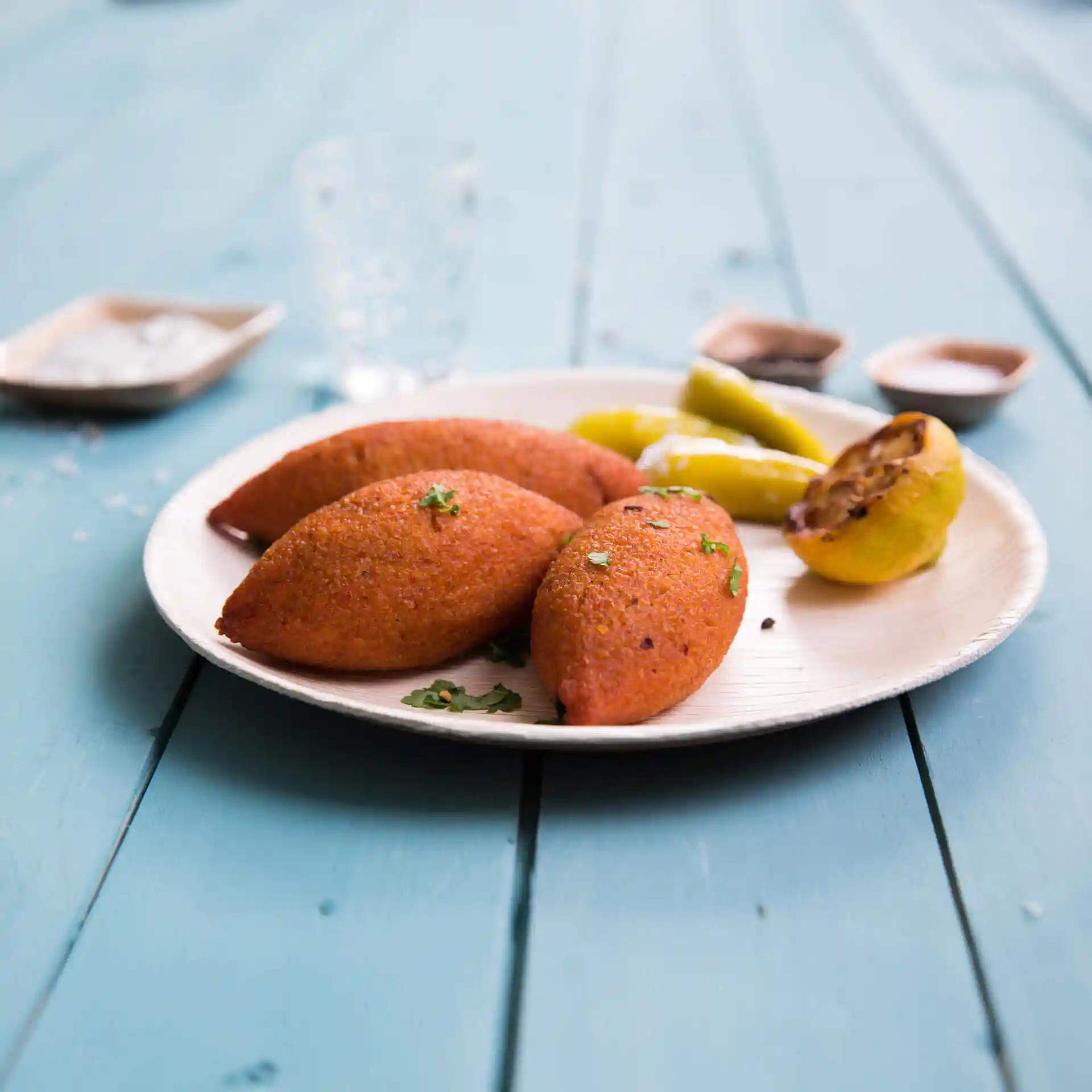 Assiette avec trois éléments de couleur orange, garnie d'herbes, accompagnée de poivrons jaunes et d'une tranche de citron grillée.