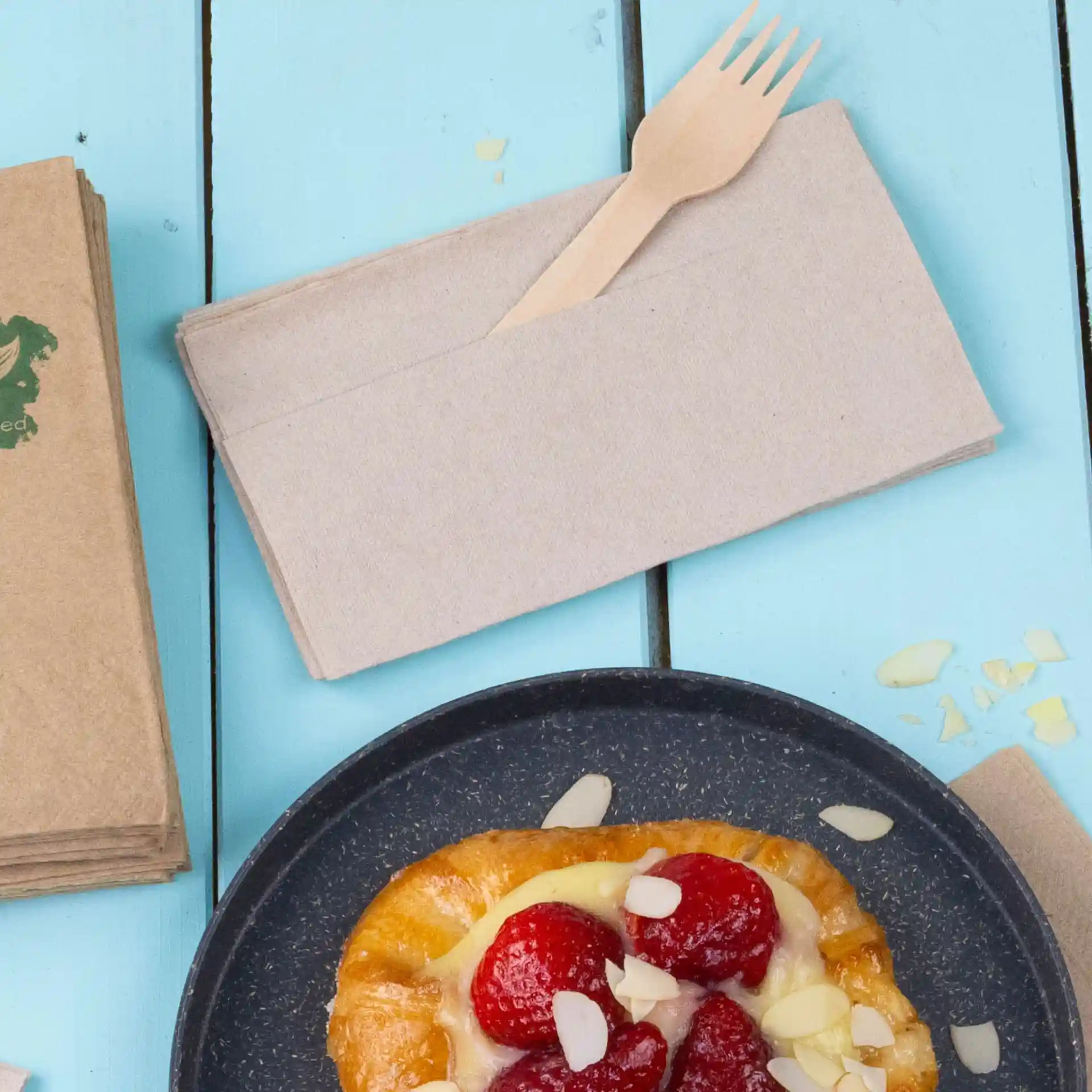 Serviette en papier non blanchie avec une fourchette en bois, placée sur une surface en bois bleu à côté d'une pâtisserie.
