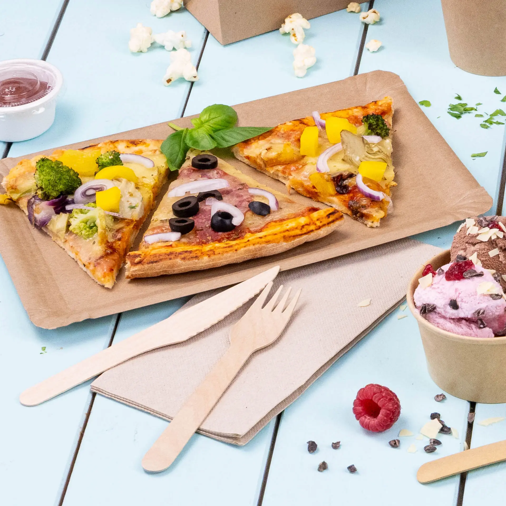 Image de trois parts de pizza avec divers garnitures sur une assiette en papier brun, accompagnées de couverts en bois et d'un verre de glace.
