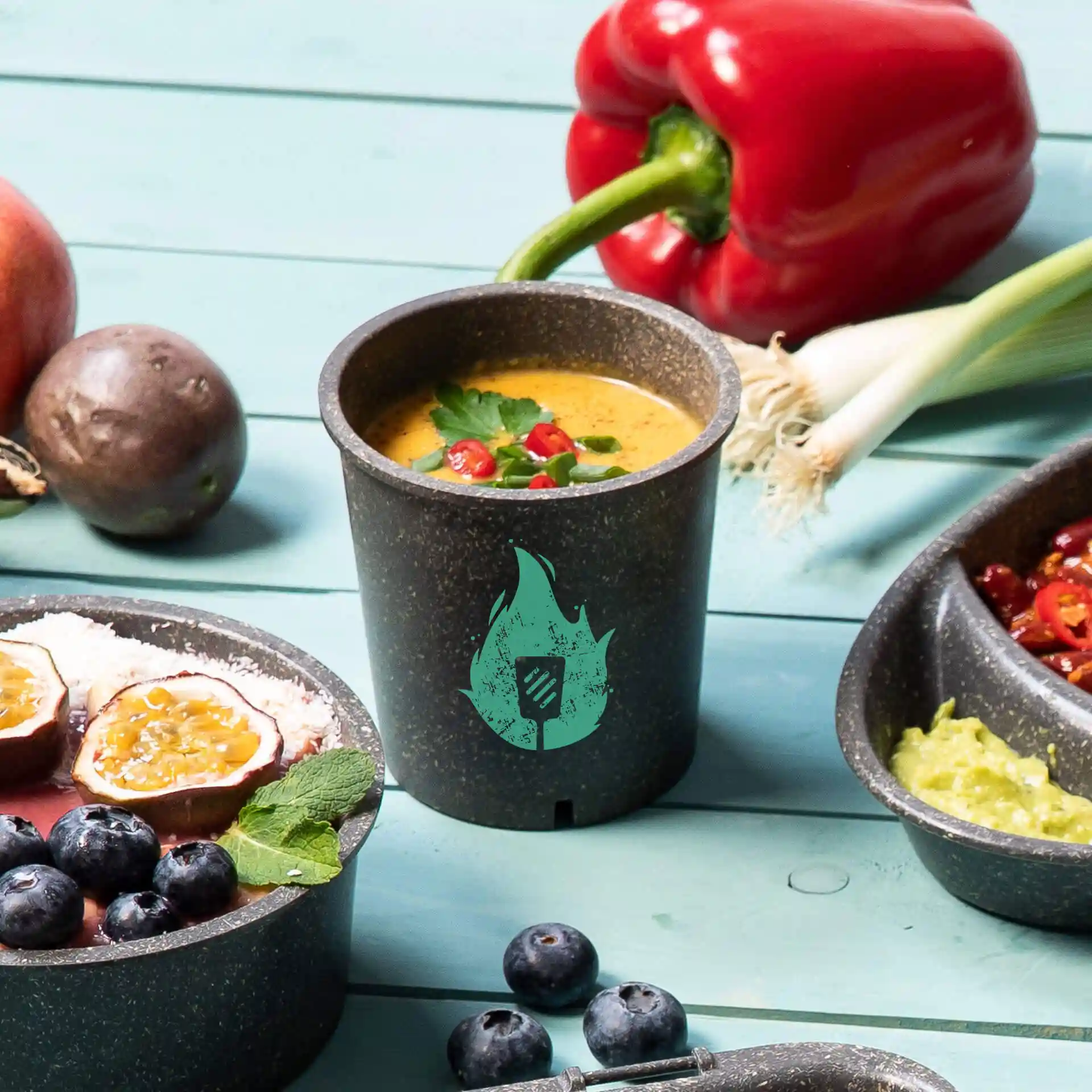 Bol rond gris réutilisable rempli de soupe jusqu'au bord, garni d'herbes et de piment, sur une surface bleue avec des aliments.