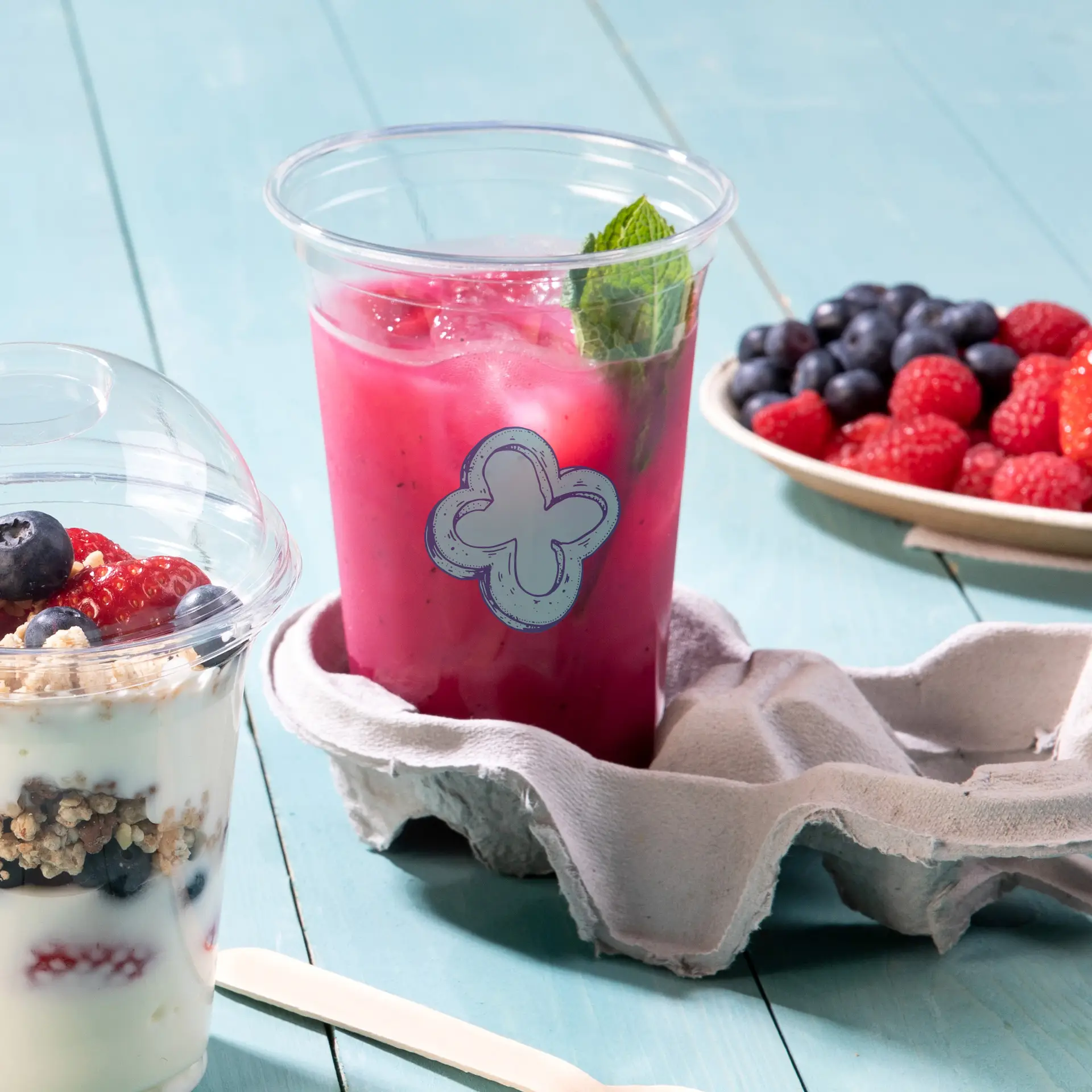 Gobelet rPET transparent de 20 oz avec une étiquette décorative bleue, rempli d'une boisson rose et garni de menthe, sur un support en tissu.