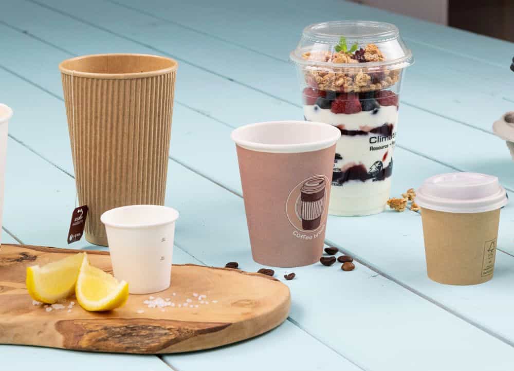 Plusieurs gobelets jetables et un dessert dans un gobelet transparent, avec des tranches de citron et du sel sur une planche en bois.