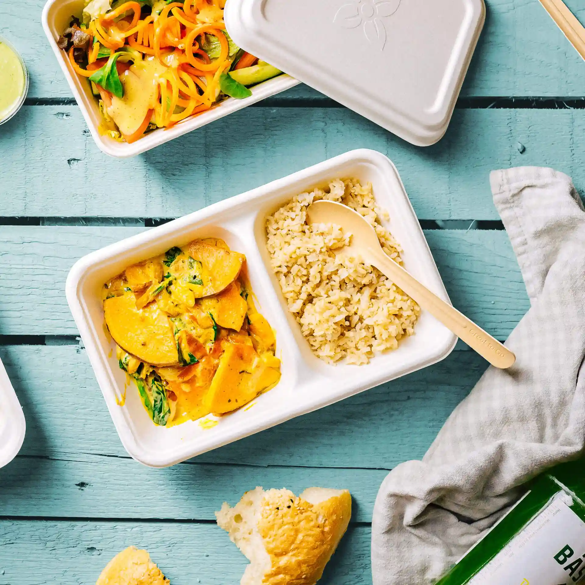 Plateau rectangulaire en canne à sucre avec deux compartiments, contenant du riz et un plat de légumes, sur une surface en bois bleu.