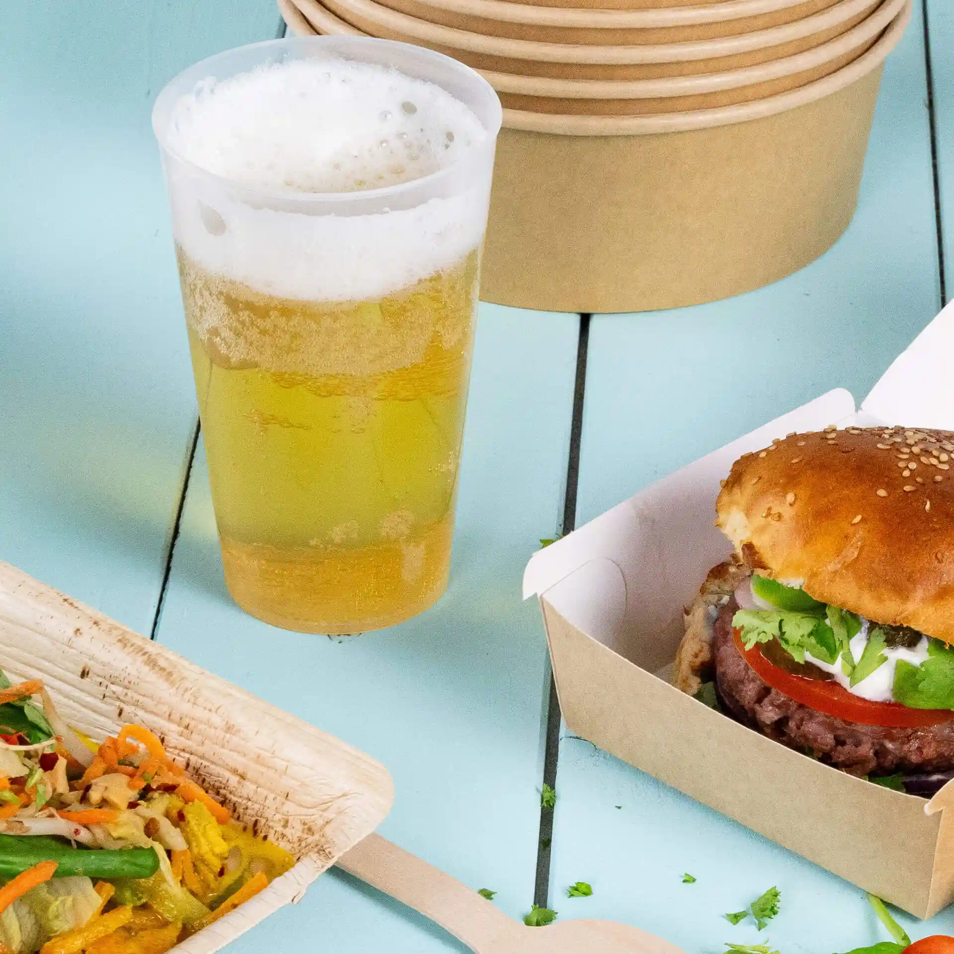 Image d'un gobelet réutilisable transparent avec de la bière, un hamburger au sésame dans une boîte et une assiette en bois avec de la salade.