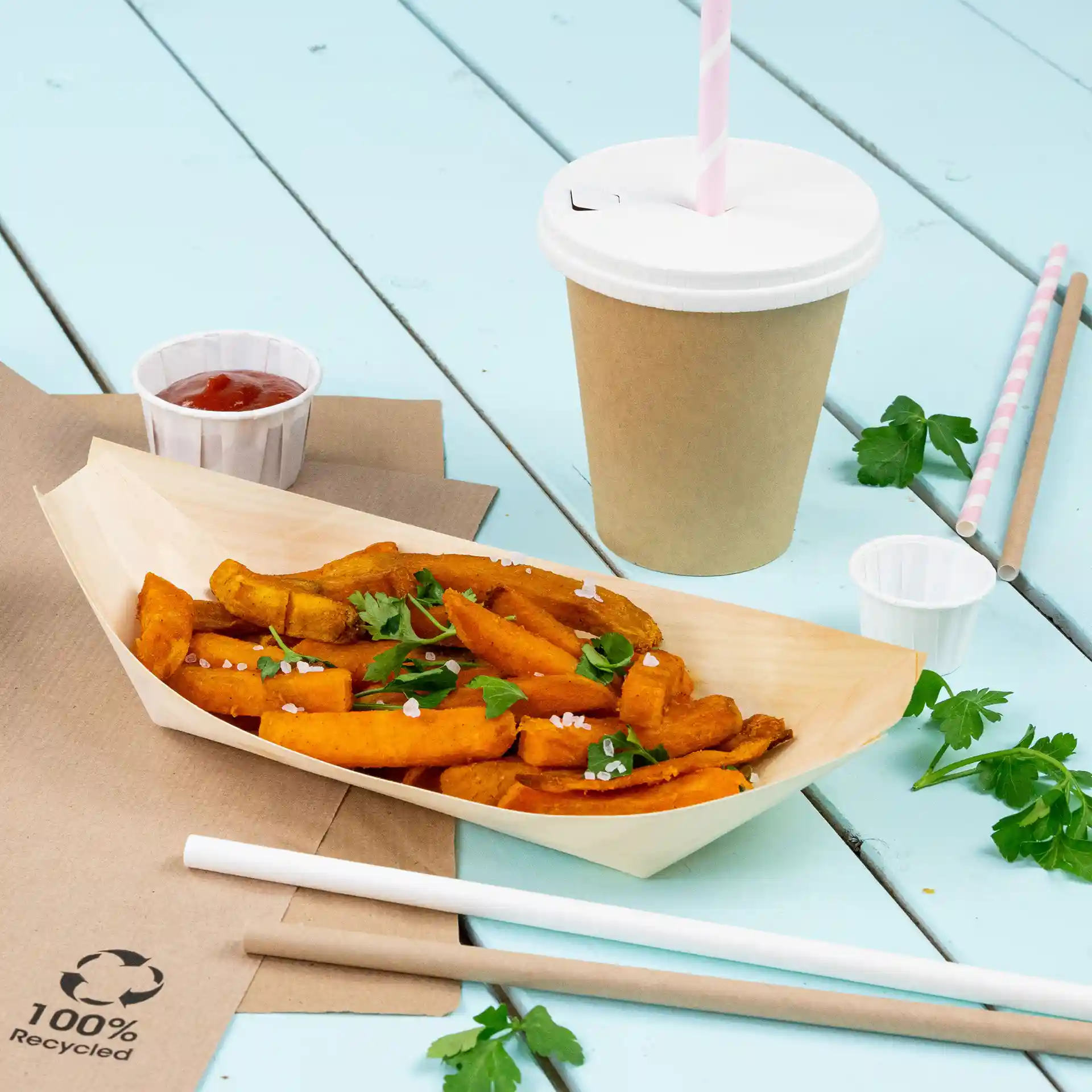 Image d'une portion de frites avec du persil, un gobelet avec une paille, un petit contenant de ketchup et des pailles en papier sur une surface bleue.