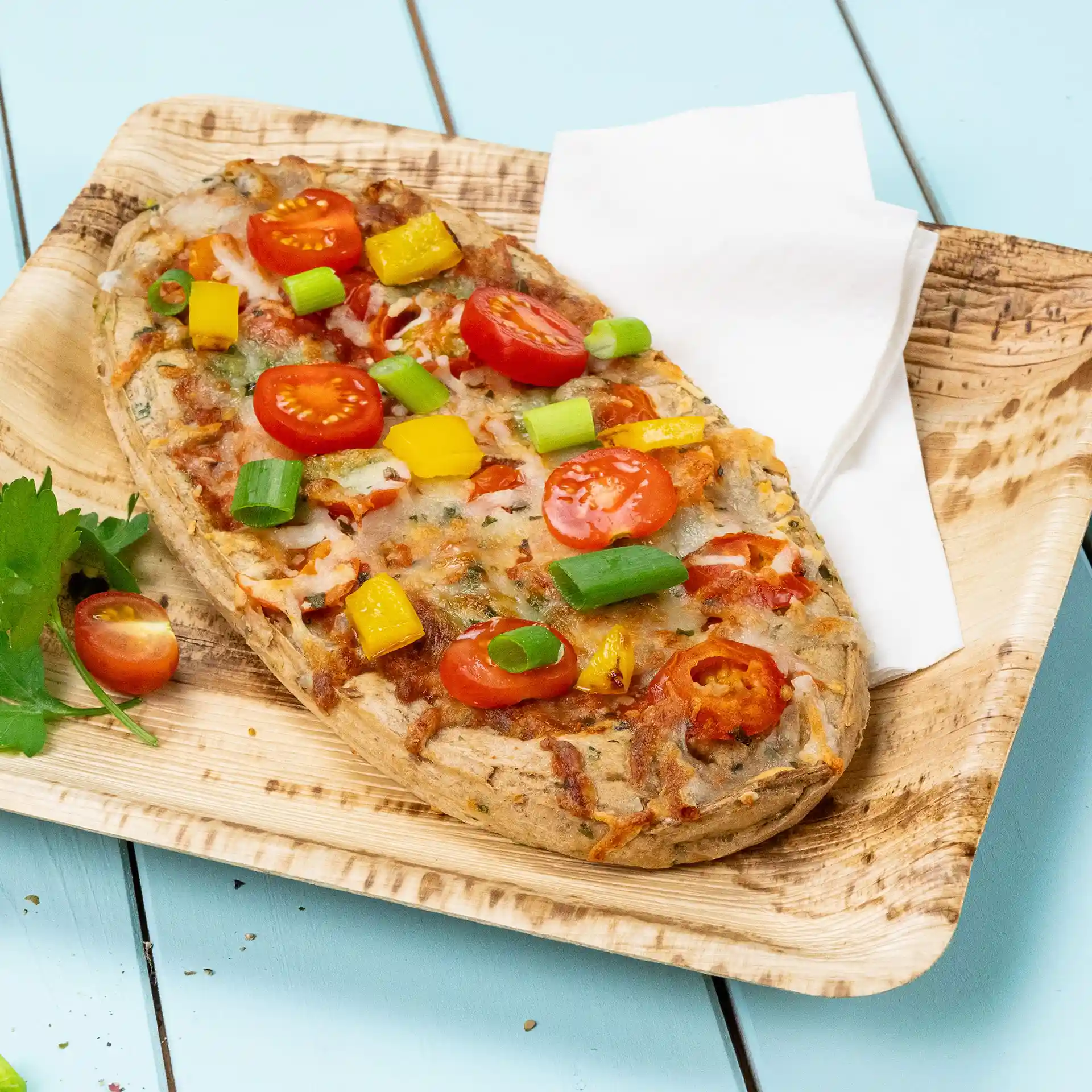 Pain plat garni de tomates cerises, poivrons jaunes et oignons verts sur une assiette en bois avec une serviette.