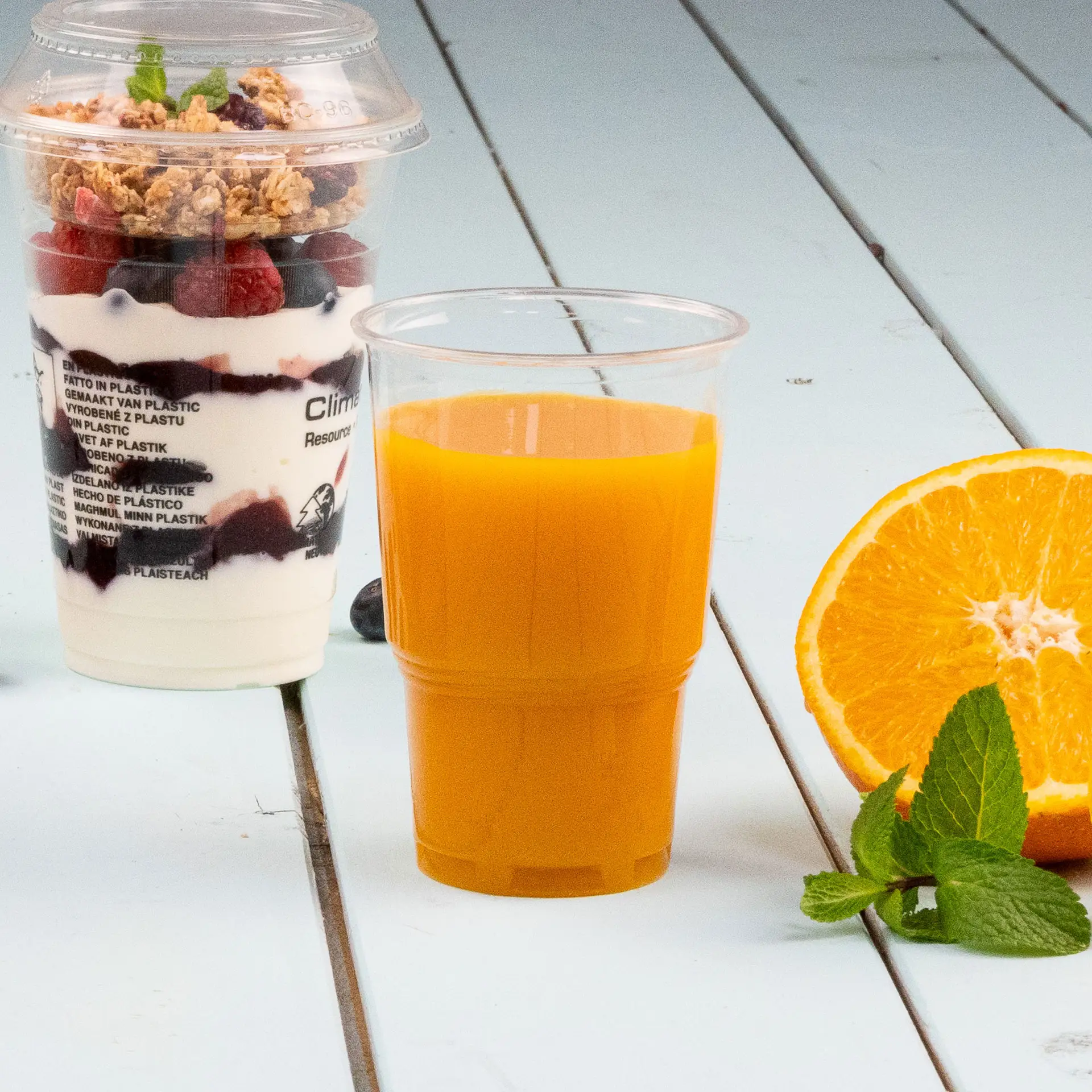 Un gobelet PLACup biodégradable transparent, 250 ml, conçu pour les boissons froides ; montré partiellement sous d'autres gobelets similaires.