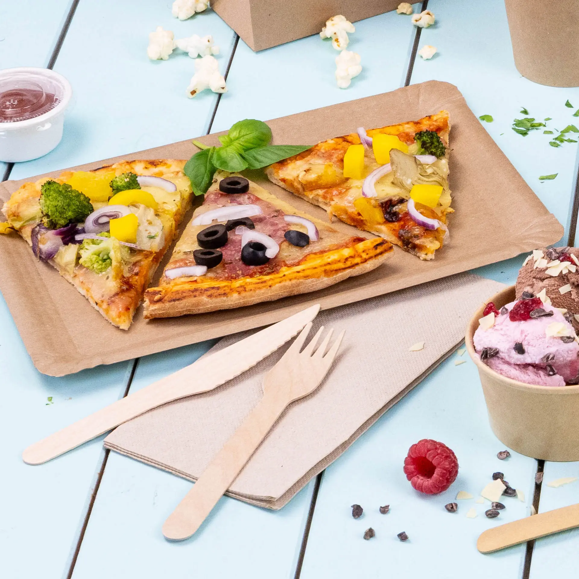 Image de trois parts de pizza sur un plateau en papier brun, avec des couverts en bois et un verre de glace à proximité.