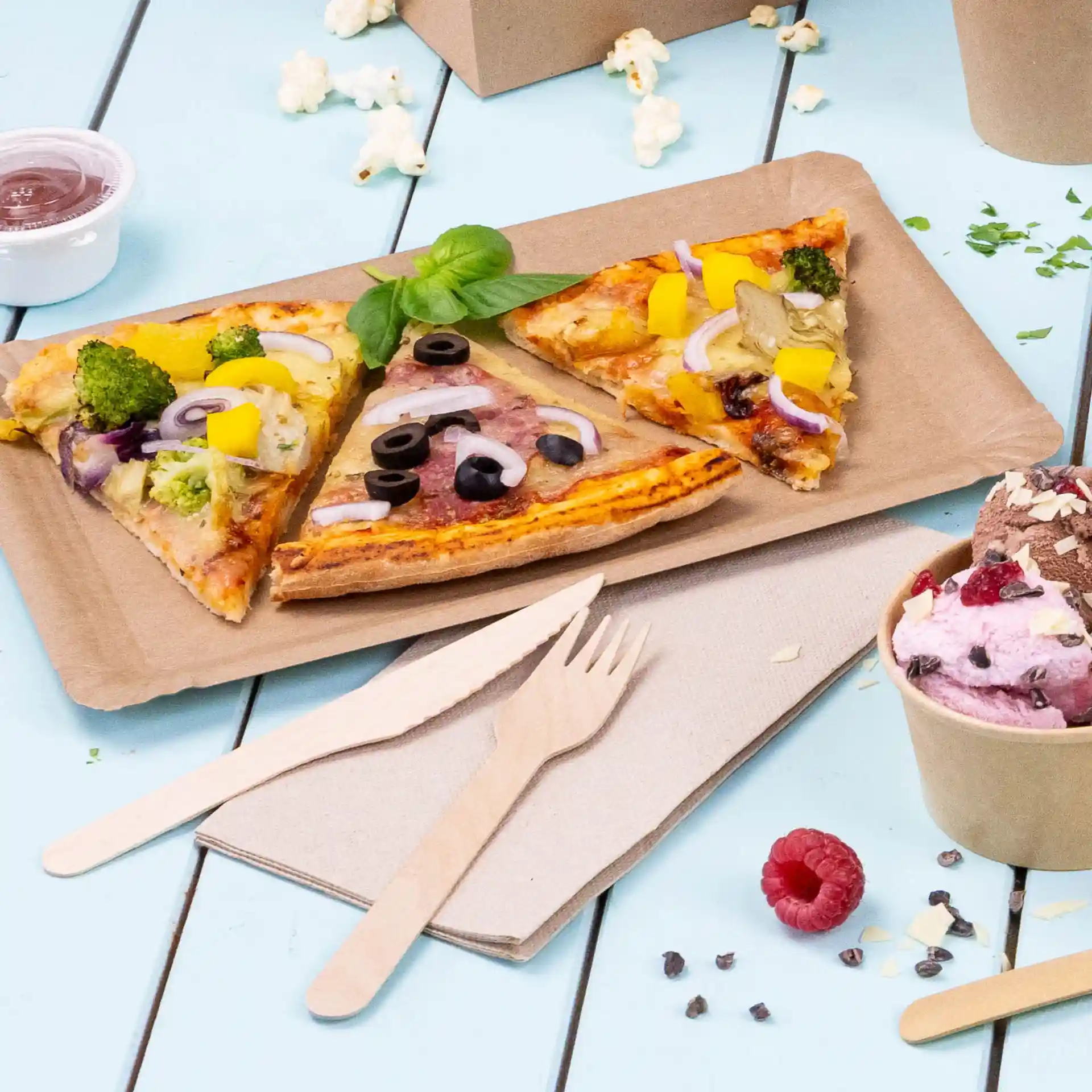 Image de trois parts de pizza sur un plateau en papier brun, avec des couverts en bois et un verre de glace à proximité.