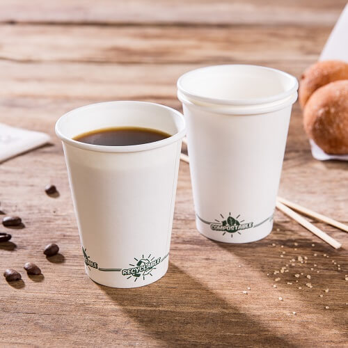 Deux gobelets en papier blancs jetables sur une surface en bois; l'un rempli de café; tous deux étiquetés "recyclable" et "compostable".