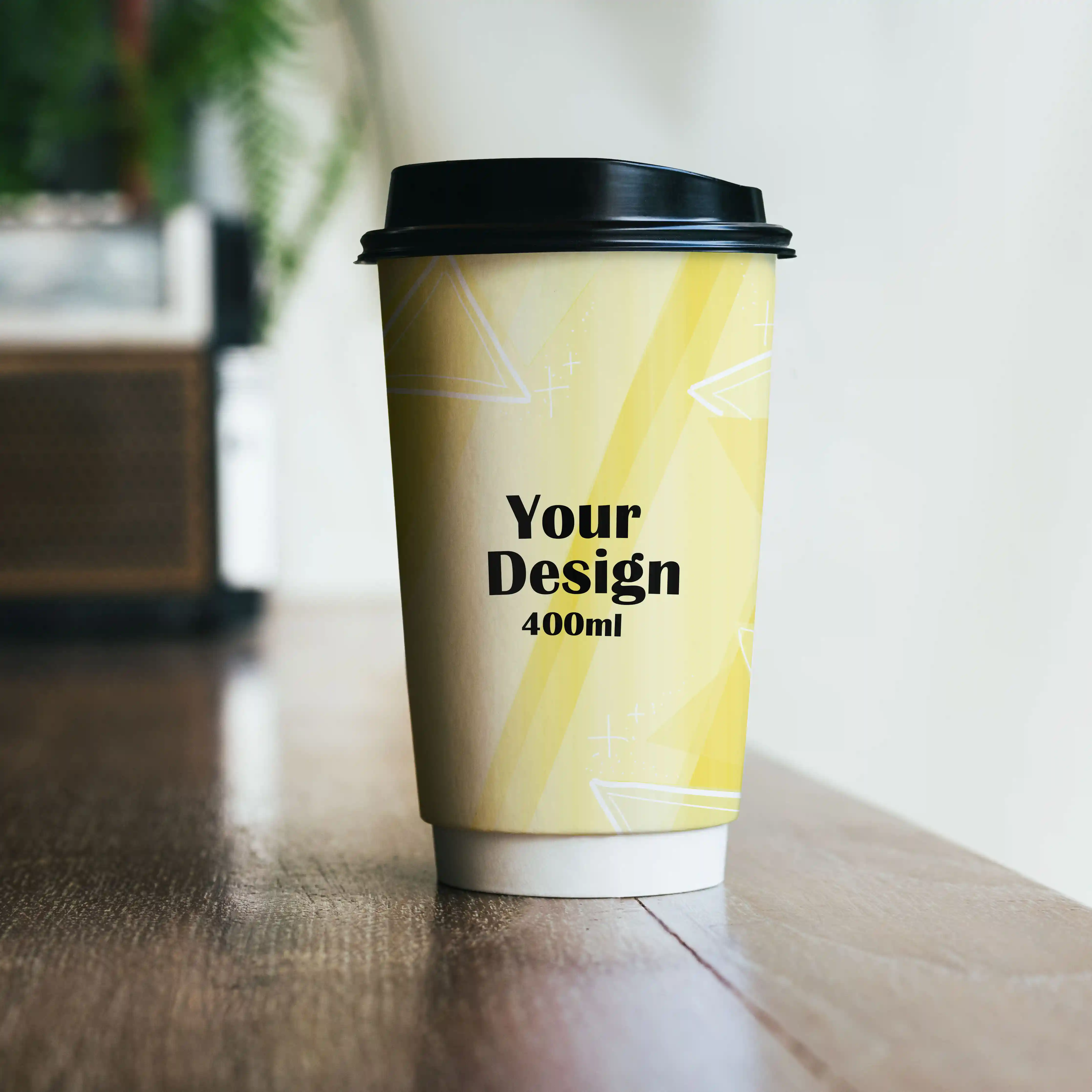 Gobelet en papier à double paroi avec un design jaune, un couvercle noir et un texte imprimé, posé sur une surface en bois.