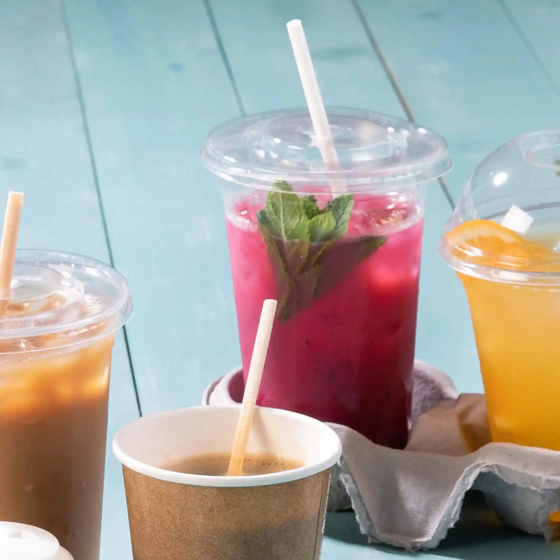 Image de plusieurs boissons dans des gobelets transparents avec des pailles, y compris une boisson rose avec des feuilles de menthe et une boisson brune dans un gobelet en papier.