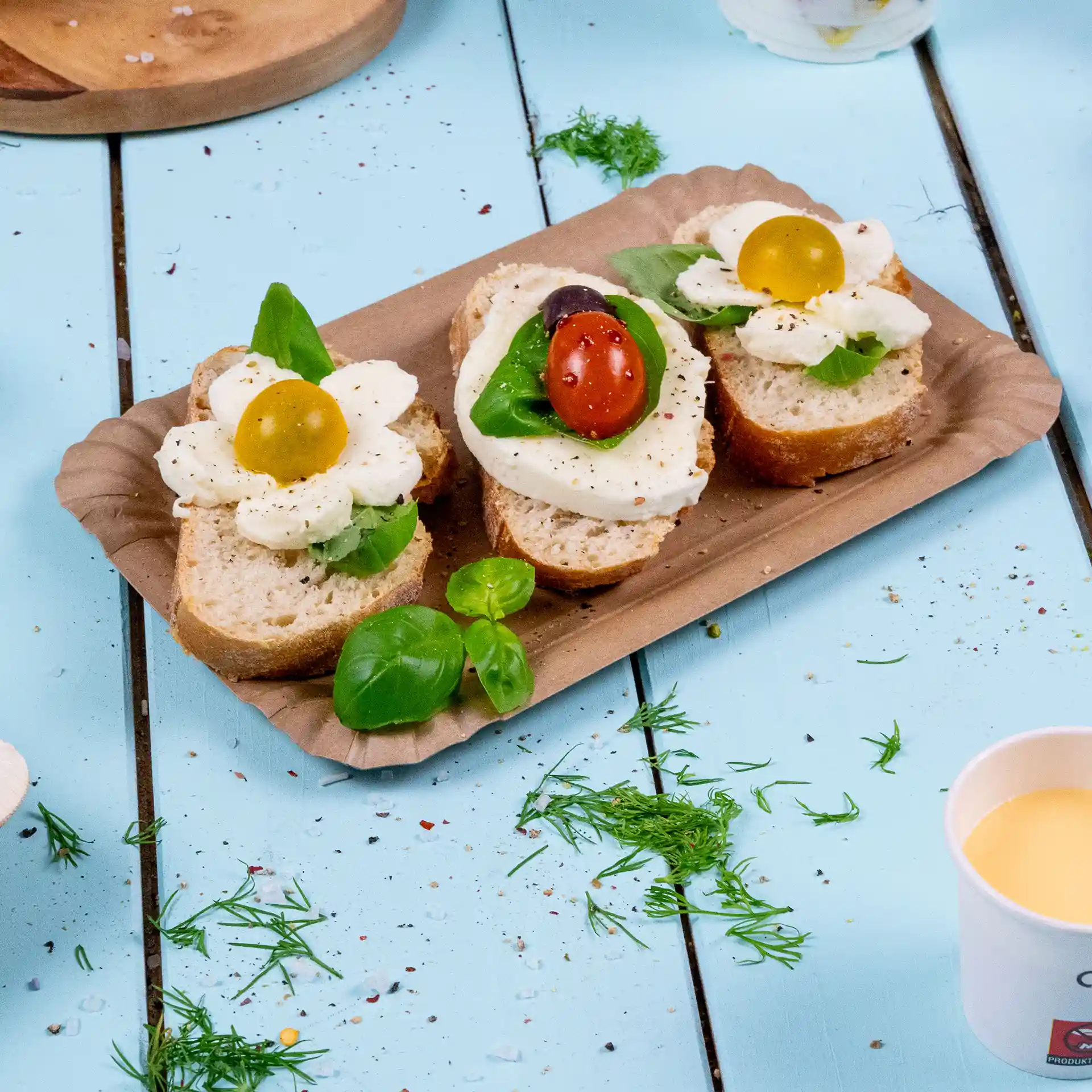 Assiette rectangulaire en carton brun avec deux tranches de pain garnies de mozzarella, basilic et tomates cerises.