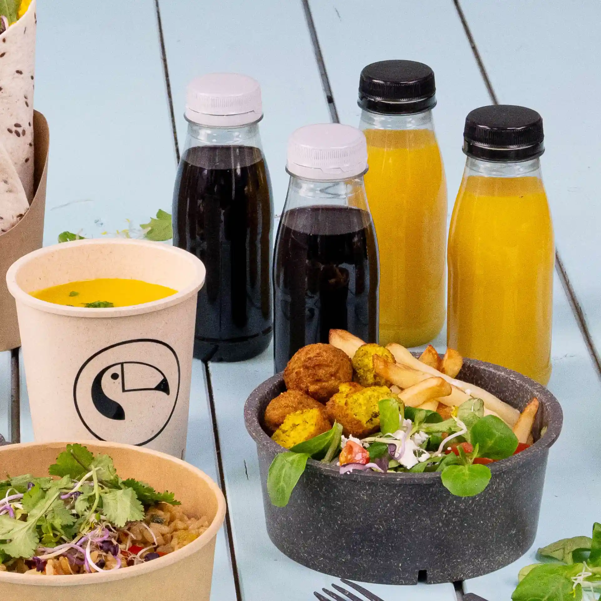 Image d'une disposition de repas avec un bol de soupe, deux assiettes de salade et falafel, et quatre bouteilles transparentes avec des couvercles noir et blanc.