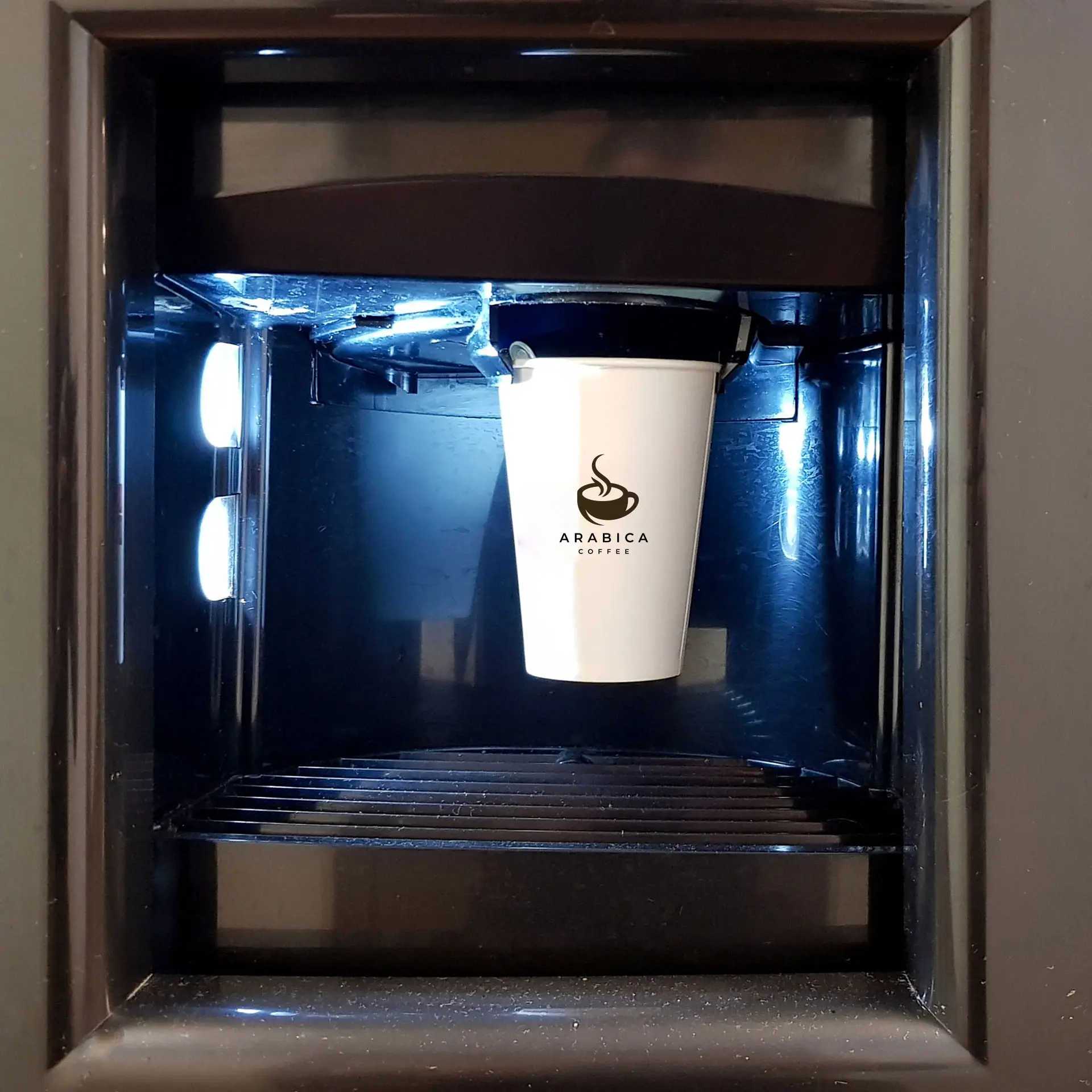 Un gobelet en papier blanc avec un logo "Arabica Coffee" dans un distributeur, éclairé par des lumières LED bleues.