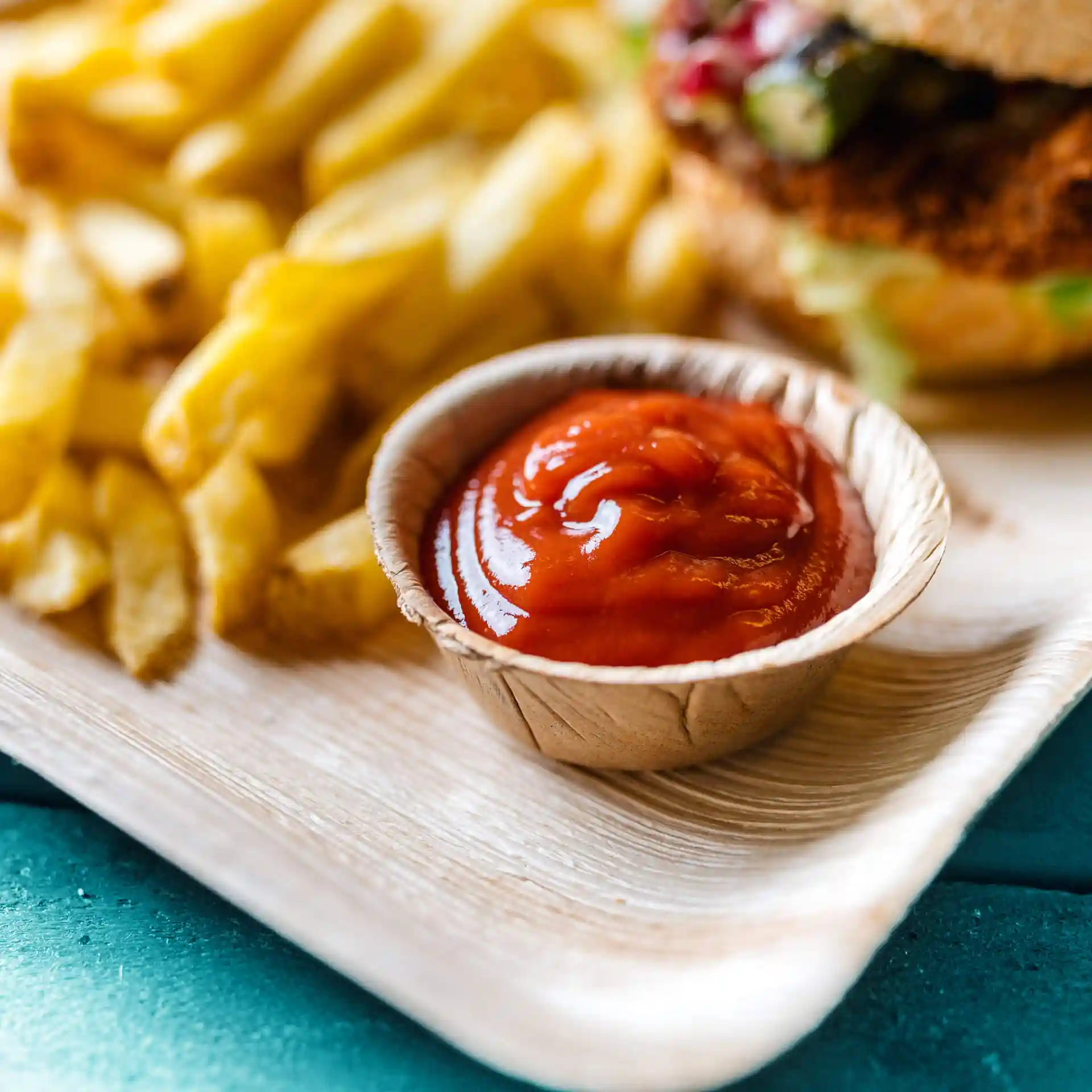 Bol en feuille de palmier contenant du ketchup, avec des frites en arrière-plan sur une surface en bois.
