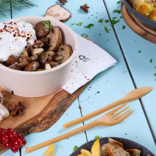 Bol avec des champignons sautés, surmontés de yaourt et d'épices, accompagné d'ustensiles en bois sur fond bleu.