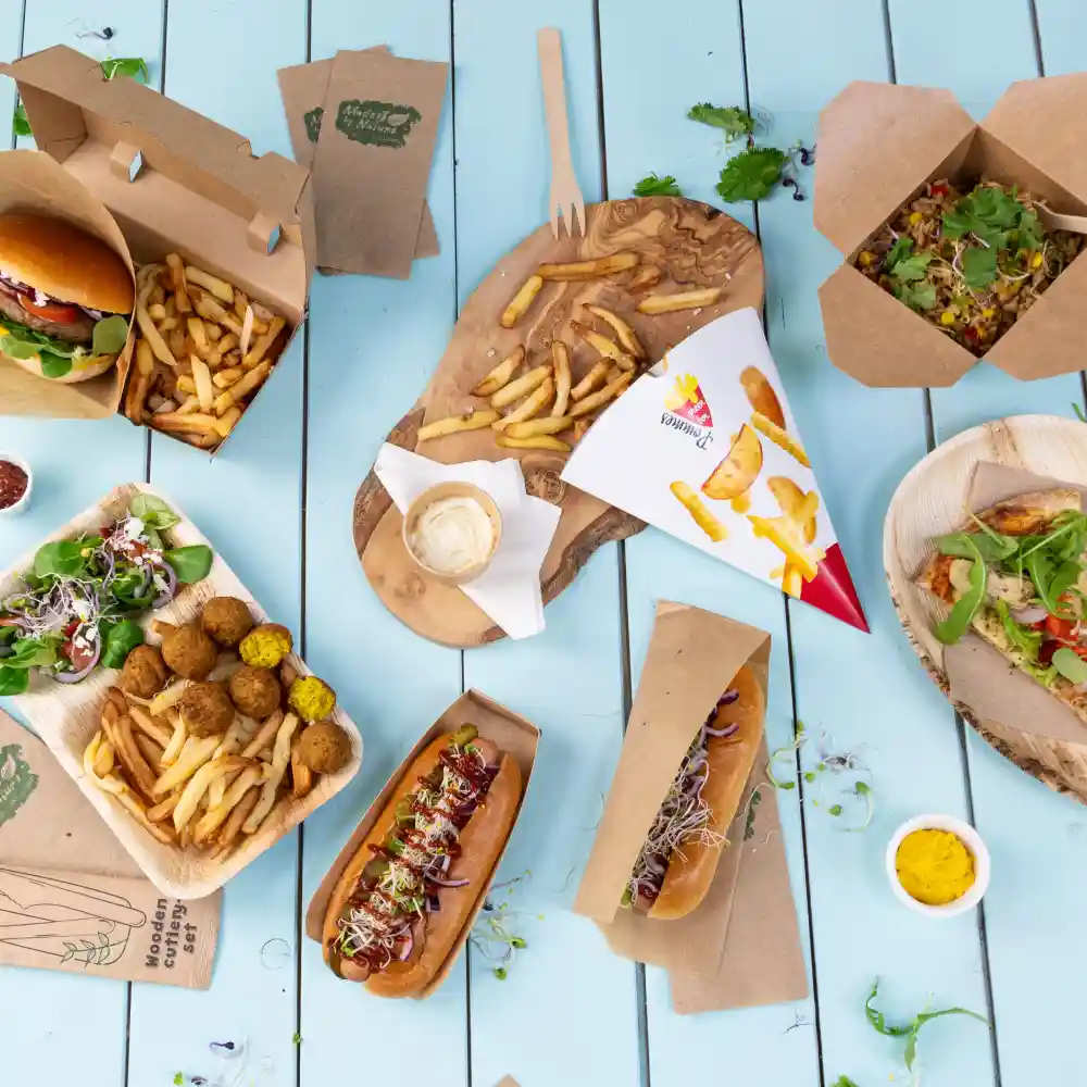 Variété d'articles de fast-food, y compris des burgers, des hot-dogs, des frites, des salades et des falafels, servis sur des plateaux en bois et en papier.