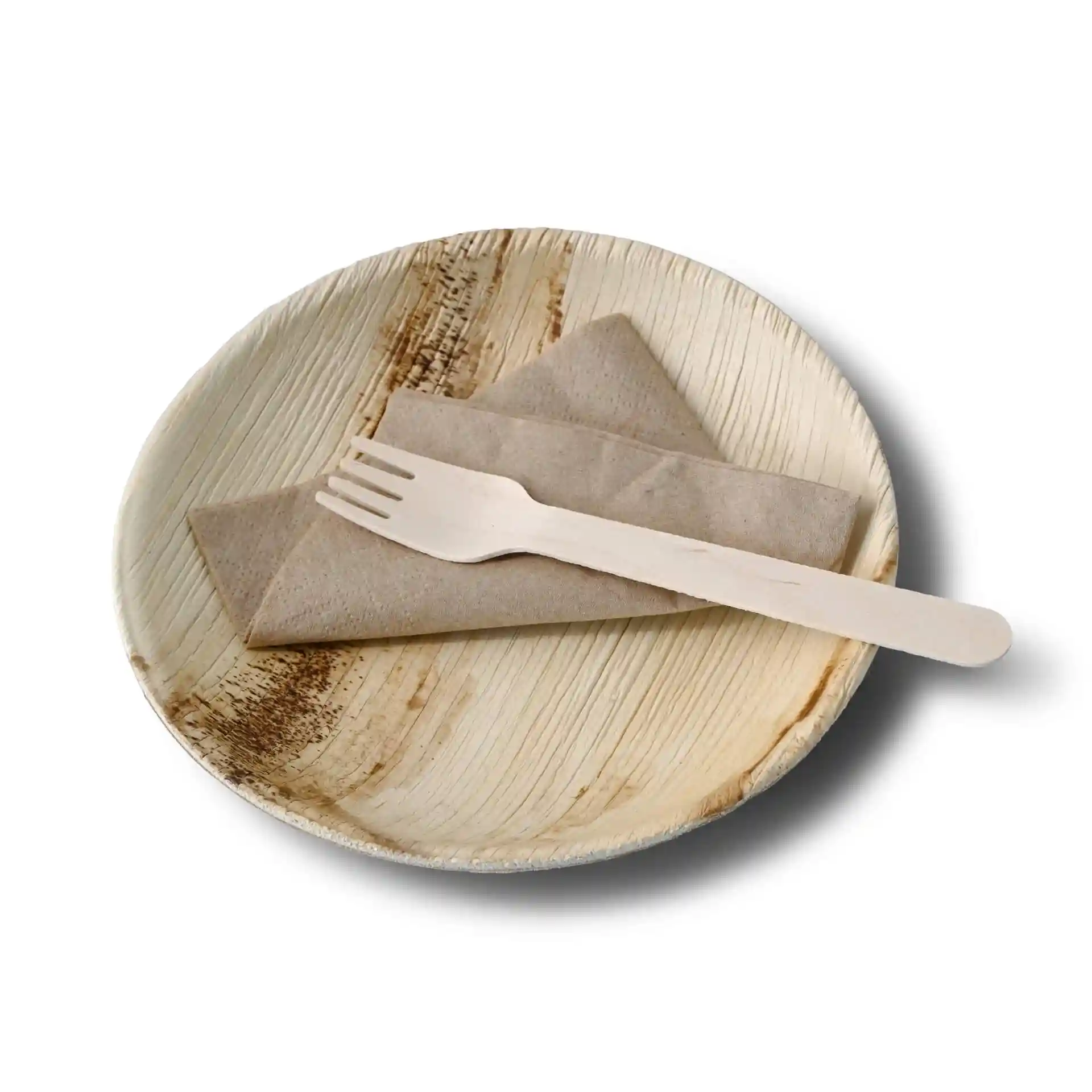 Assiette ronde en feuille de palmier avec une texture grainée, une serviette brune pliée et une fourchette en bois dessus.