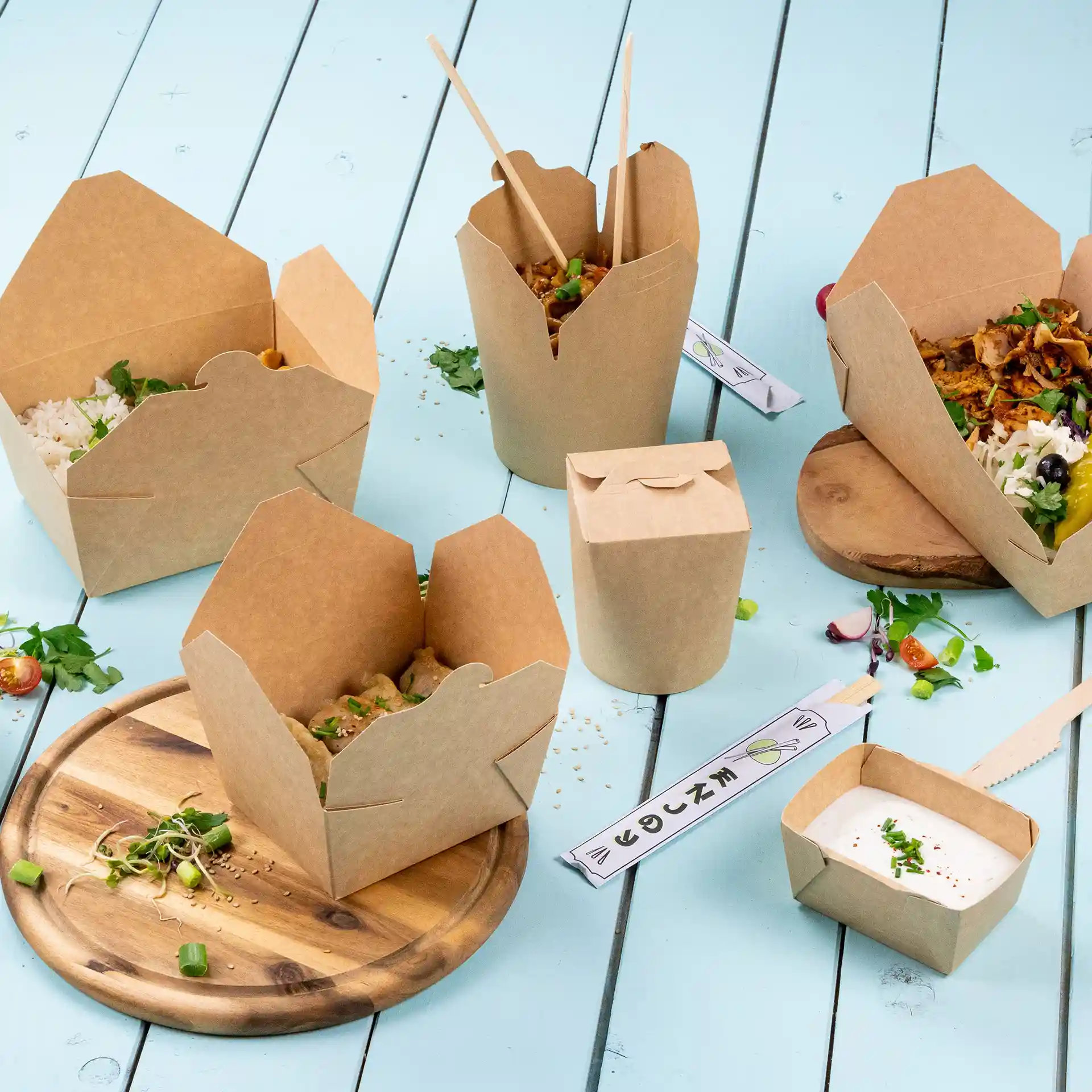 Image de plusieurs boîtes en carton brunes à emporter avec de la nourriture, placées sur une surface bleu clair et une planche en bois.