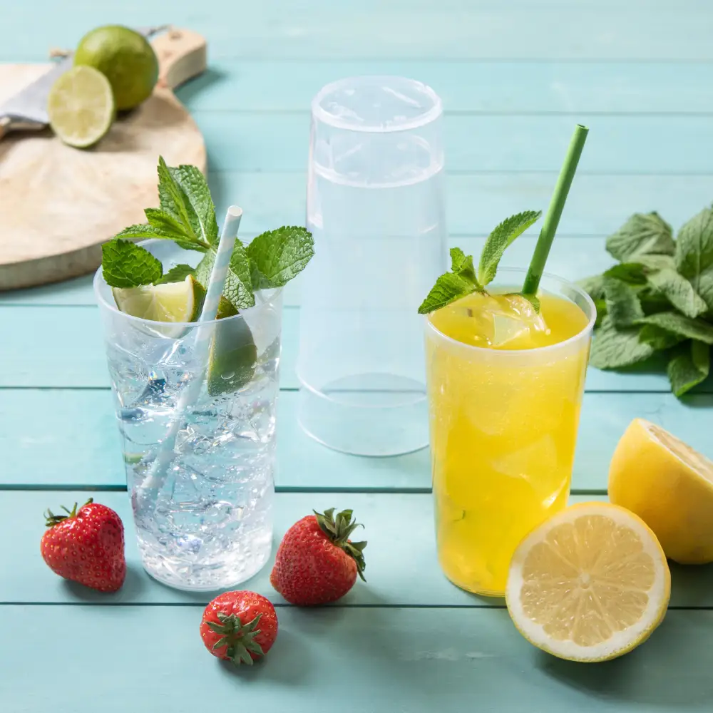 Deux boissons dans des verres transparents avec de la menthe et des fruits, entourées de fraises et d'un demi-citron sur une surface en bois.