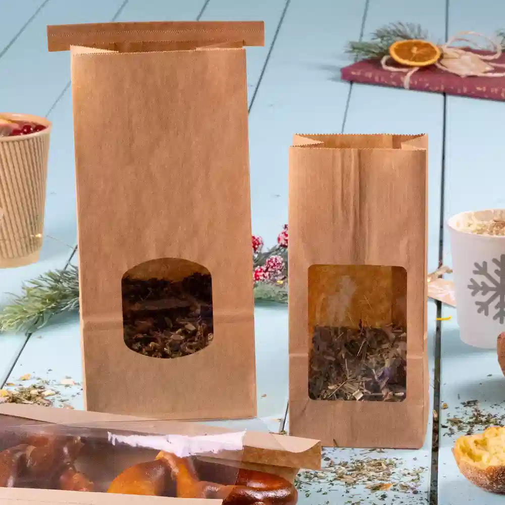 Deux sachets en papier brun avec des fenêtres transparentes, l'un plus grand et l'autre plus petit, contenant des herbes ou des feuilles de thé.