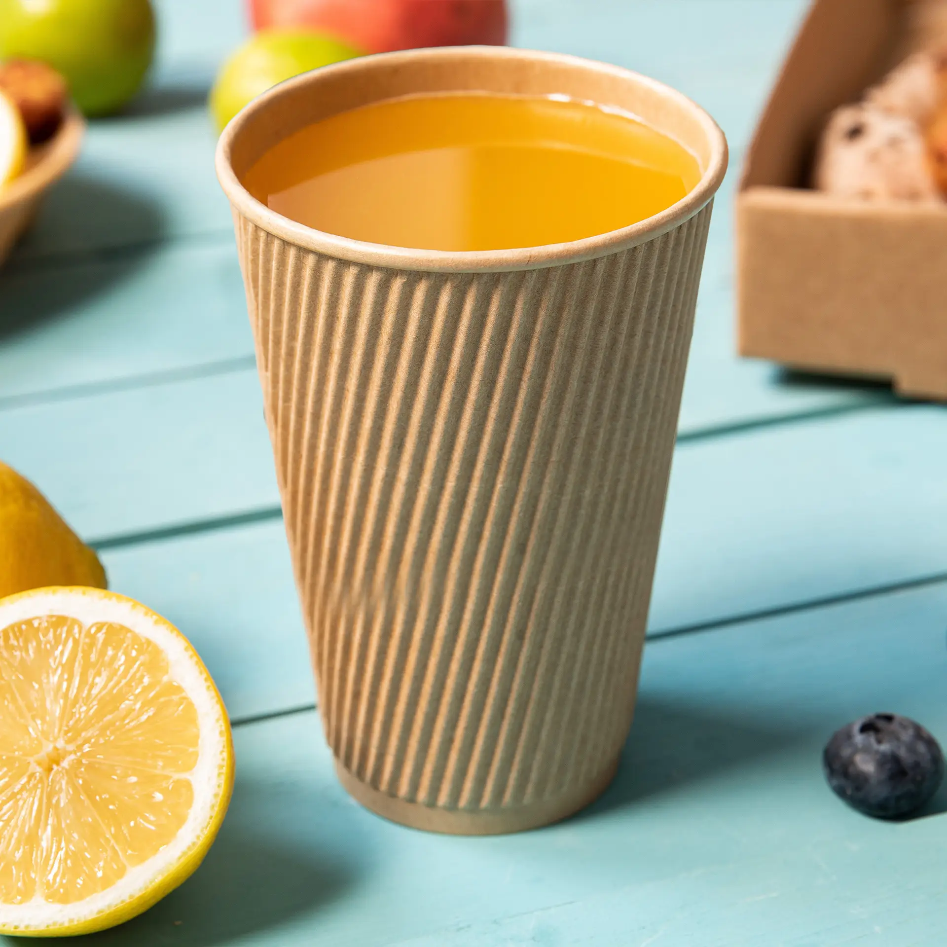 Tasse brune à triple paroi rayée, remplie d'une boisson jaune, placée sur une surface en bois bleu près d'une tranche de citron.
