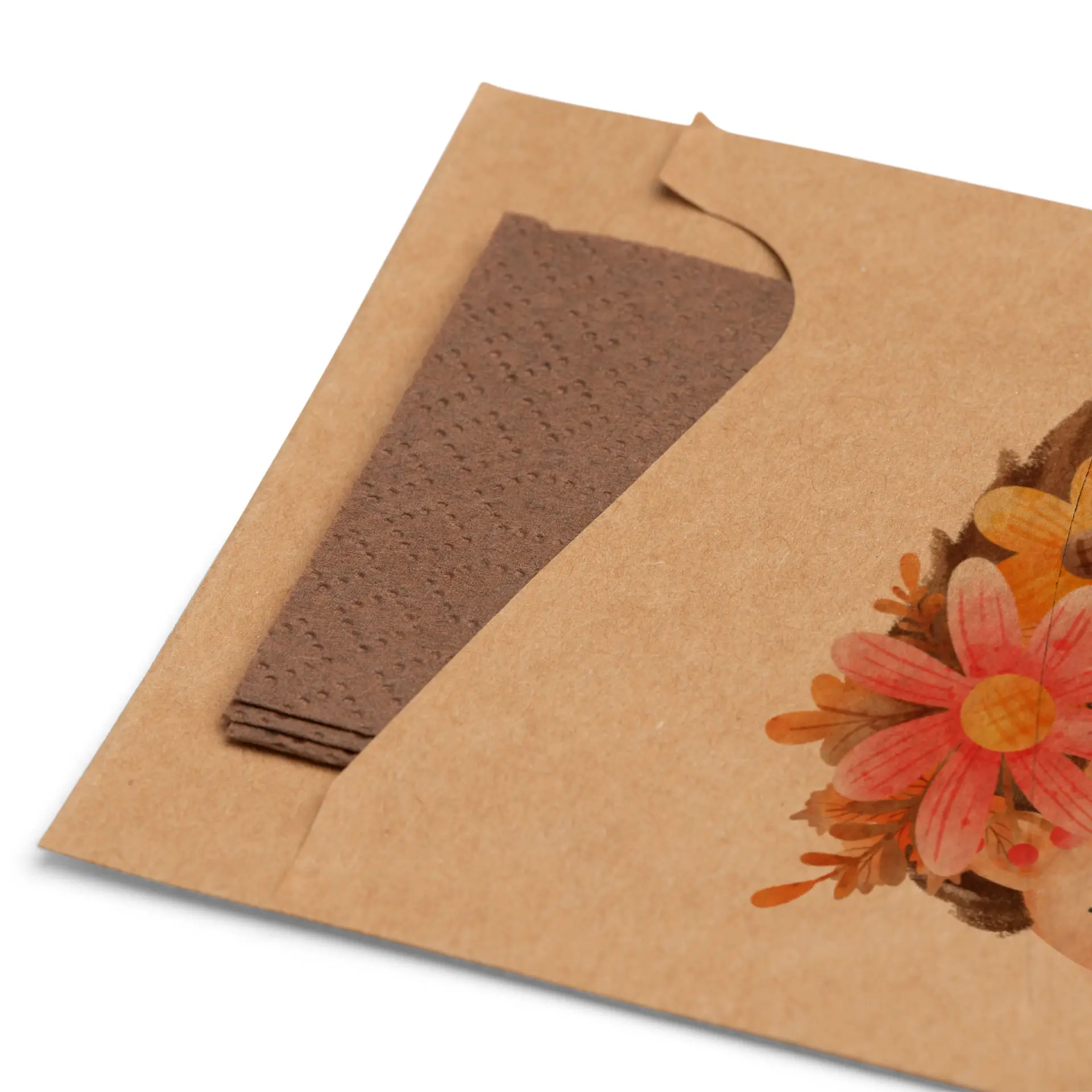 Manchon en kraft marron pour couverts avec serviette marron pliée partiellement visible, présentant un motif floral à l'avant.