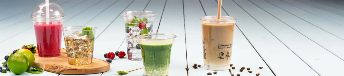 Boissons assorties exposées sur une surface en bois, y compris café glacé, smoothie, parfait de yaourt et jus, avec une tranche d'orange à proximité.