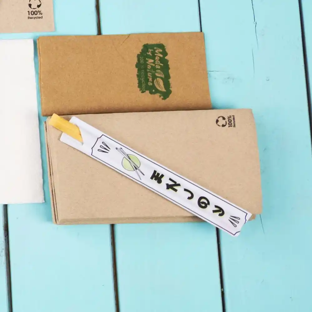 Baguettes enroulées dans du papier sur une surface en bois bleue, avec une boîte en papier kraft marron en arrière-plan.