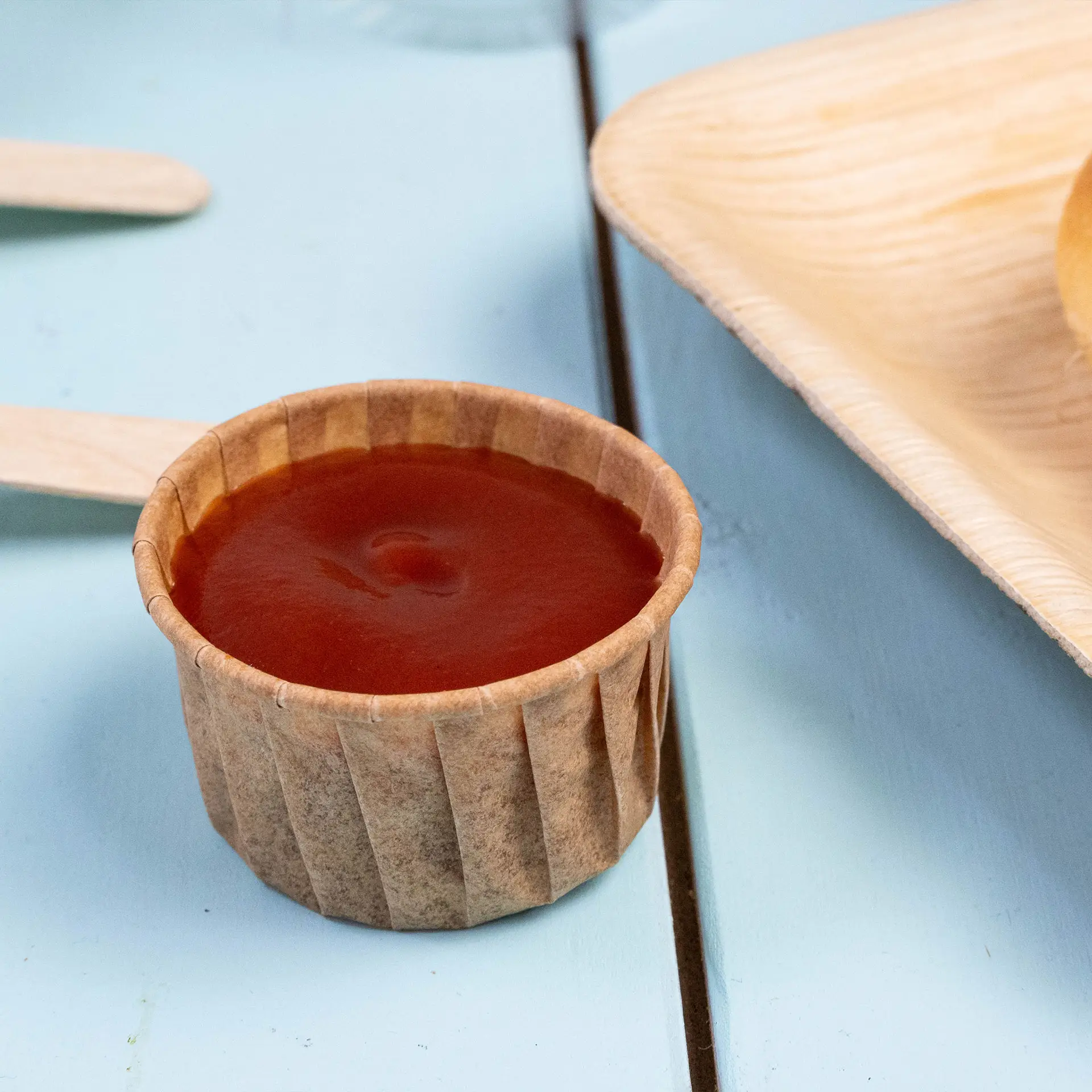Gobelet en papier brun rempli de ketchup sur une surface bleue, conçu pour les sauces et les petites portions.