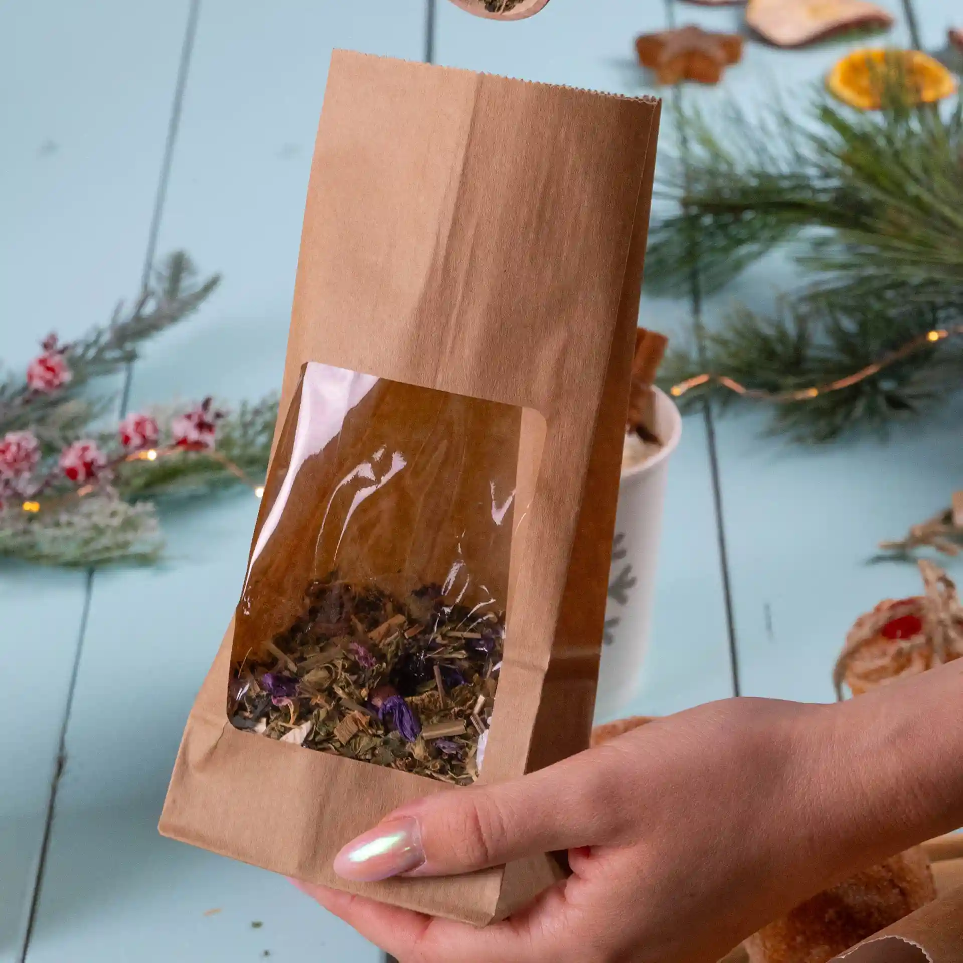 Sac en papier kraft marron avec une fenêtre transparente, contenant des herbes séchées, tenu par une main.