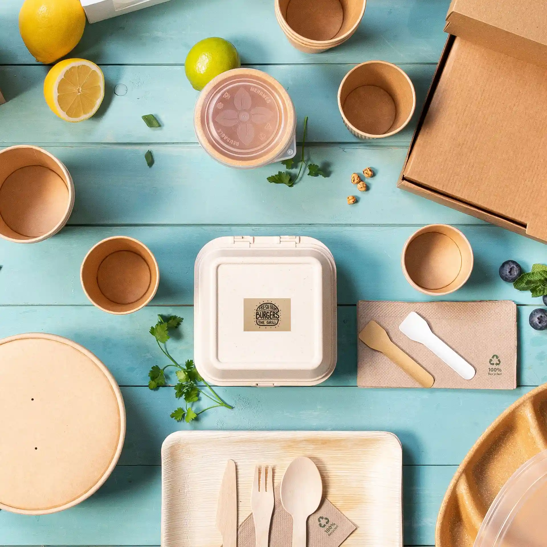 Image de divers contenants alimentaires jetables, ustensiles et garnitures sur une surface en bois bleu.