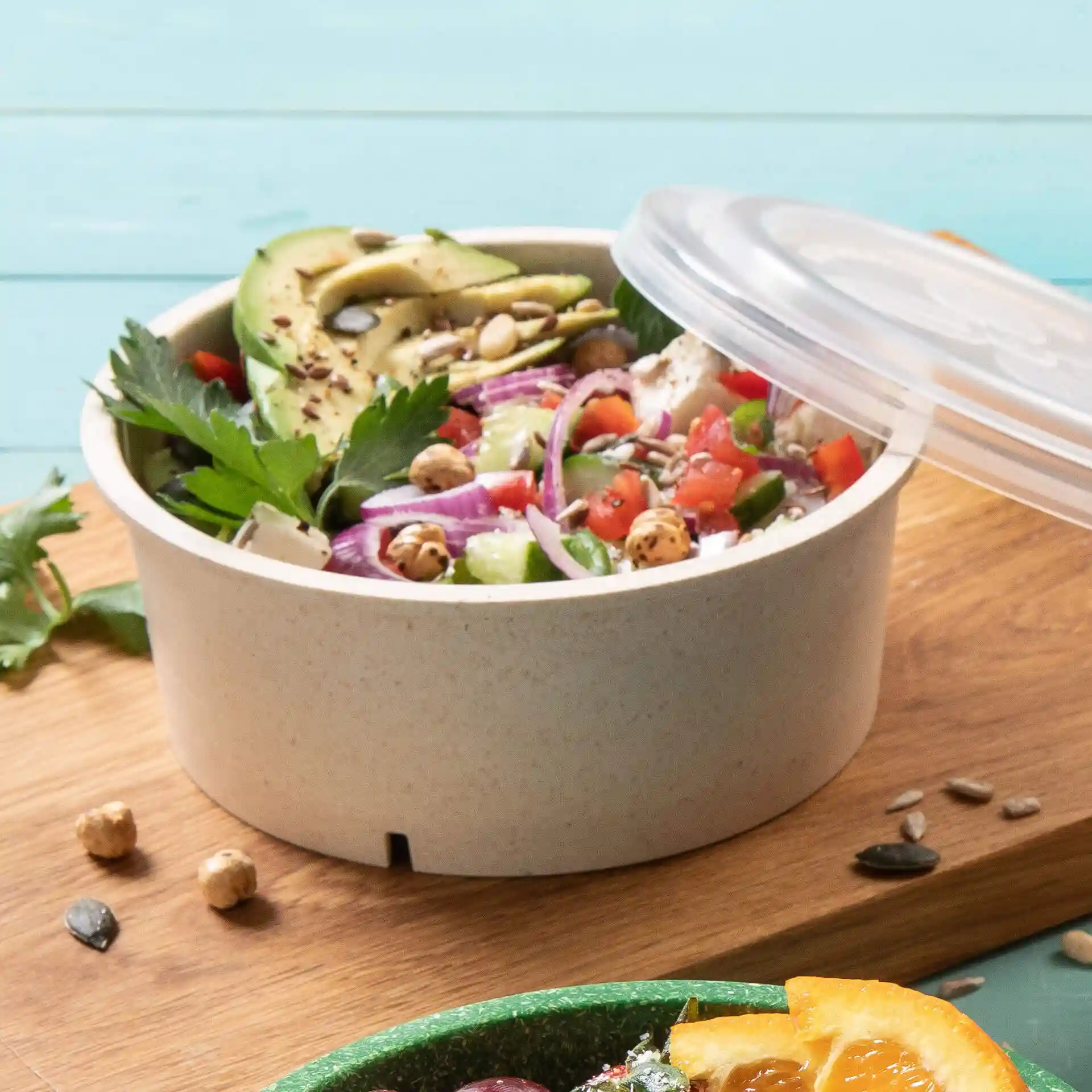 Bol rond réutilisable de couleur blanc crémeux, rempli de salade et garni de légumes, sur une surface en bois.