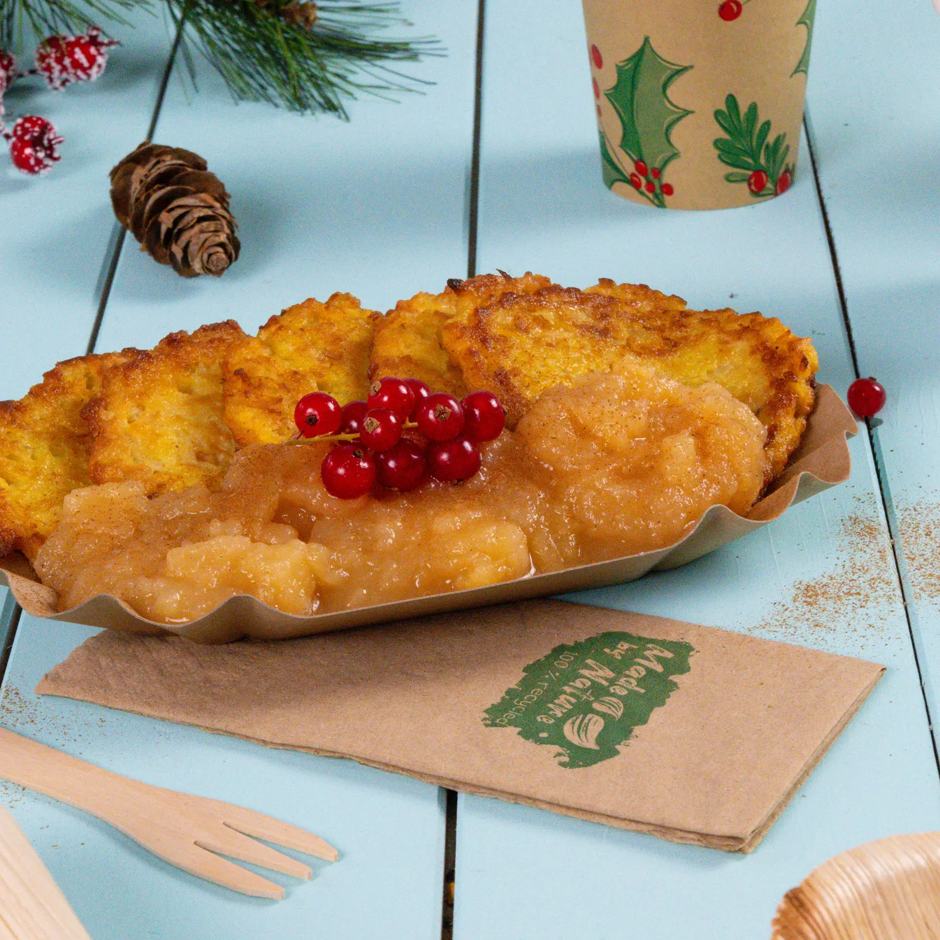 Une assiette de plats frits et de compote de pommes garnie de baies rouges ; entourée de décorations festives et de serviettes.