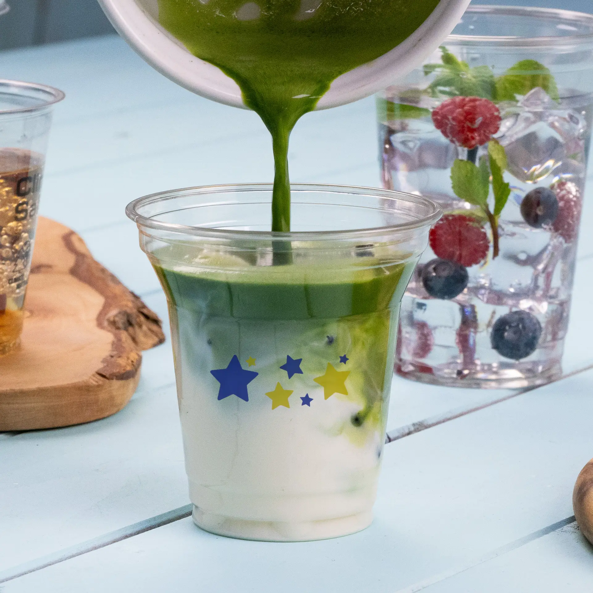 Verser une boisson verte dans un gobelet clair rPET de 8 oz avec des motifs d'étoiles ; d'autres boissons en arrière-plan.