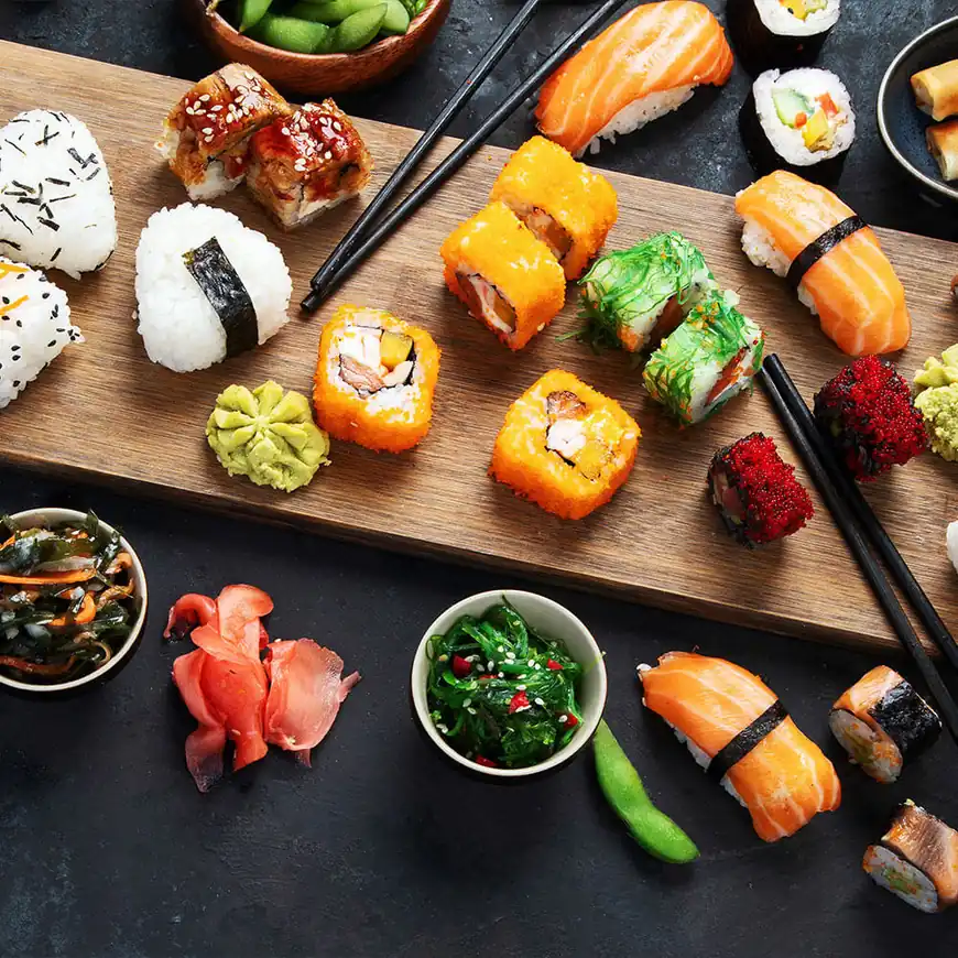 Un plat en bois avec divers types de sushi, y compris des rouleaux, sashimi et nigiri. Accompagné de wasabi, gingembre mariné et petits bols de salade d'algues.