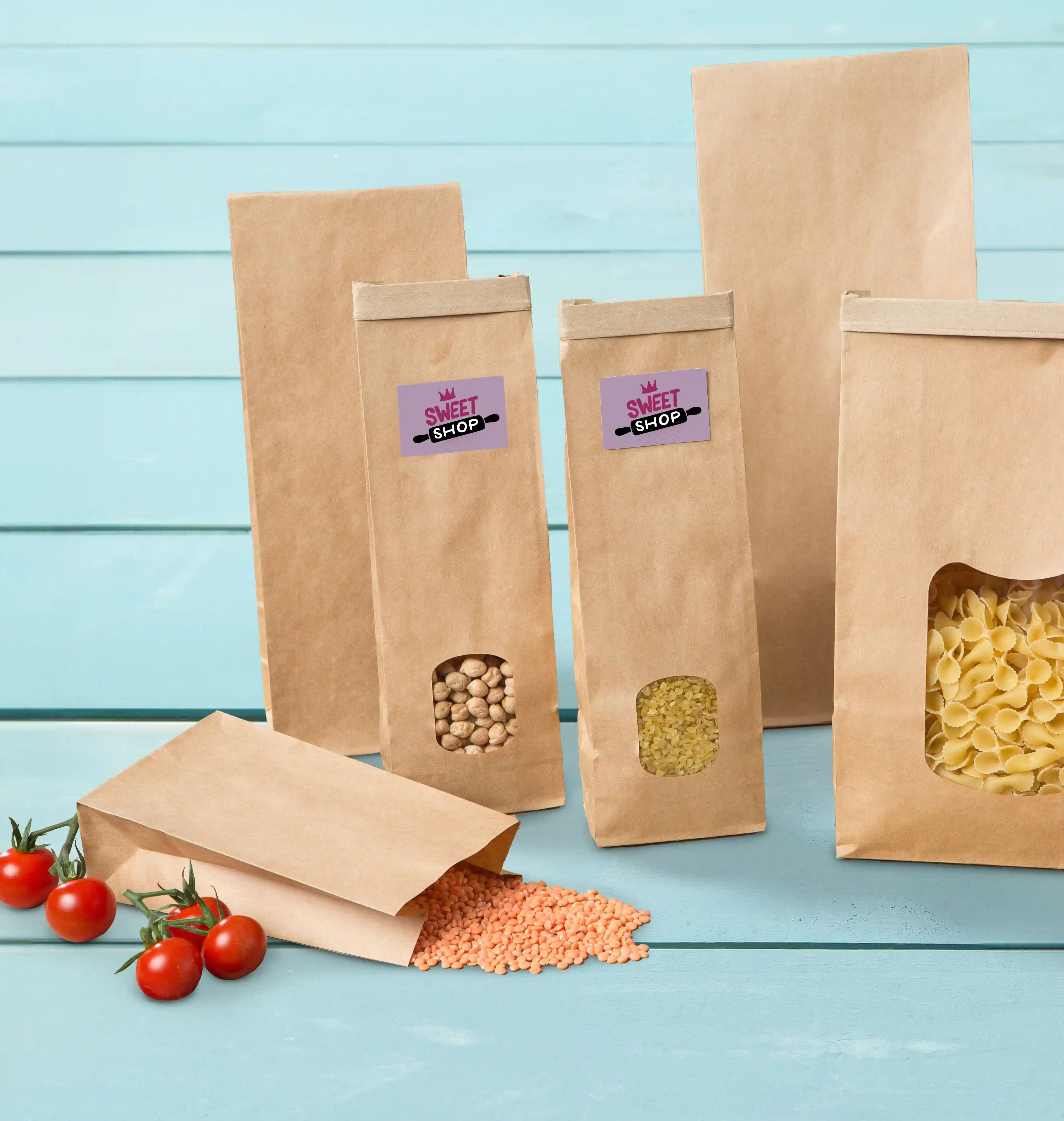 Sacs en papier brun avec fenêtres transparentes, contenant divers grains, placés sur une surface bleue avec des tomates cerises.