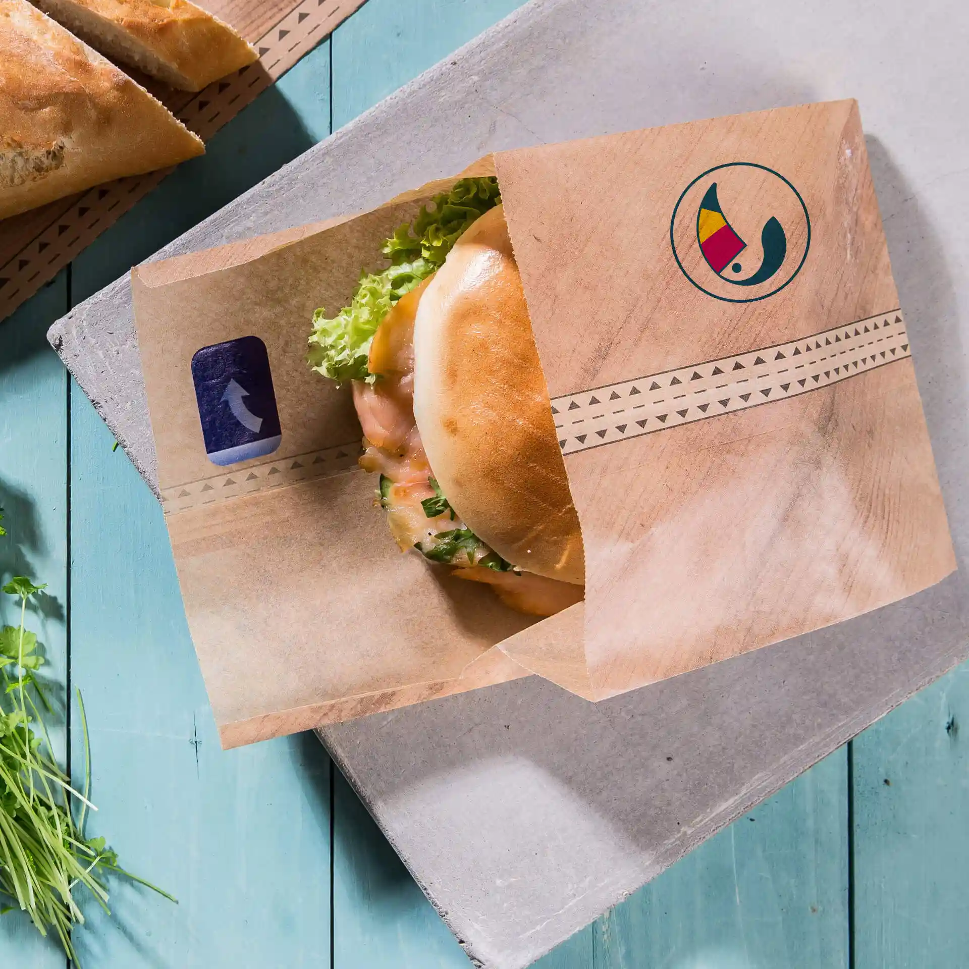 Manchette à burger personnalisée marron avec fermeture adhésive, tenant un burger avec de la laitue, sur une surface en bois bleu.