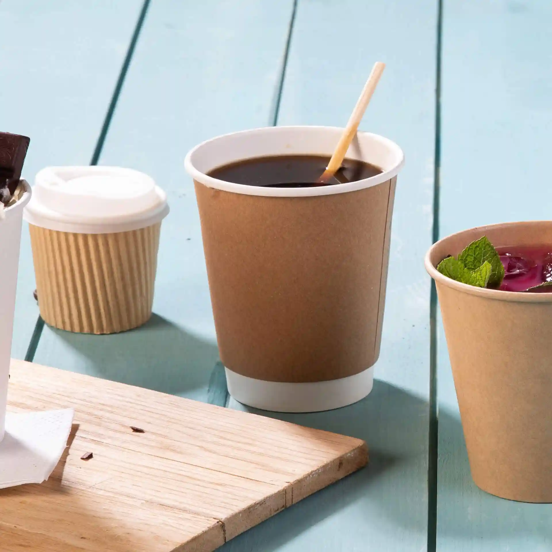 Gobelet en carton double paroi marron avec un intérieur blanc, posé sur une surface en bois avec d'autres gobelets.