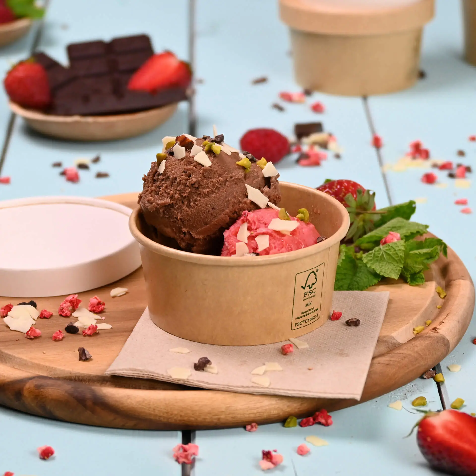 Deux boules de glace au chocolat et à la fraise avec des garnitures dans un gobelet en papier brun ; décoré de menthe et de fraises.