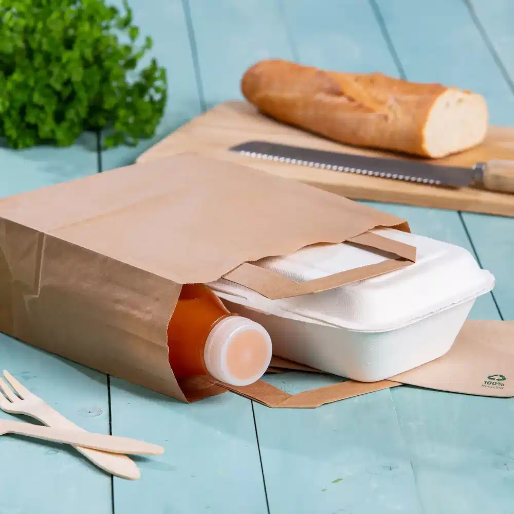 Sac en papier brun contenant une bouteille de boisson et un contenant de nourriture à emporter sur une surface en bois bleue.