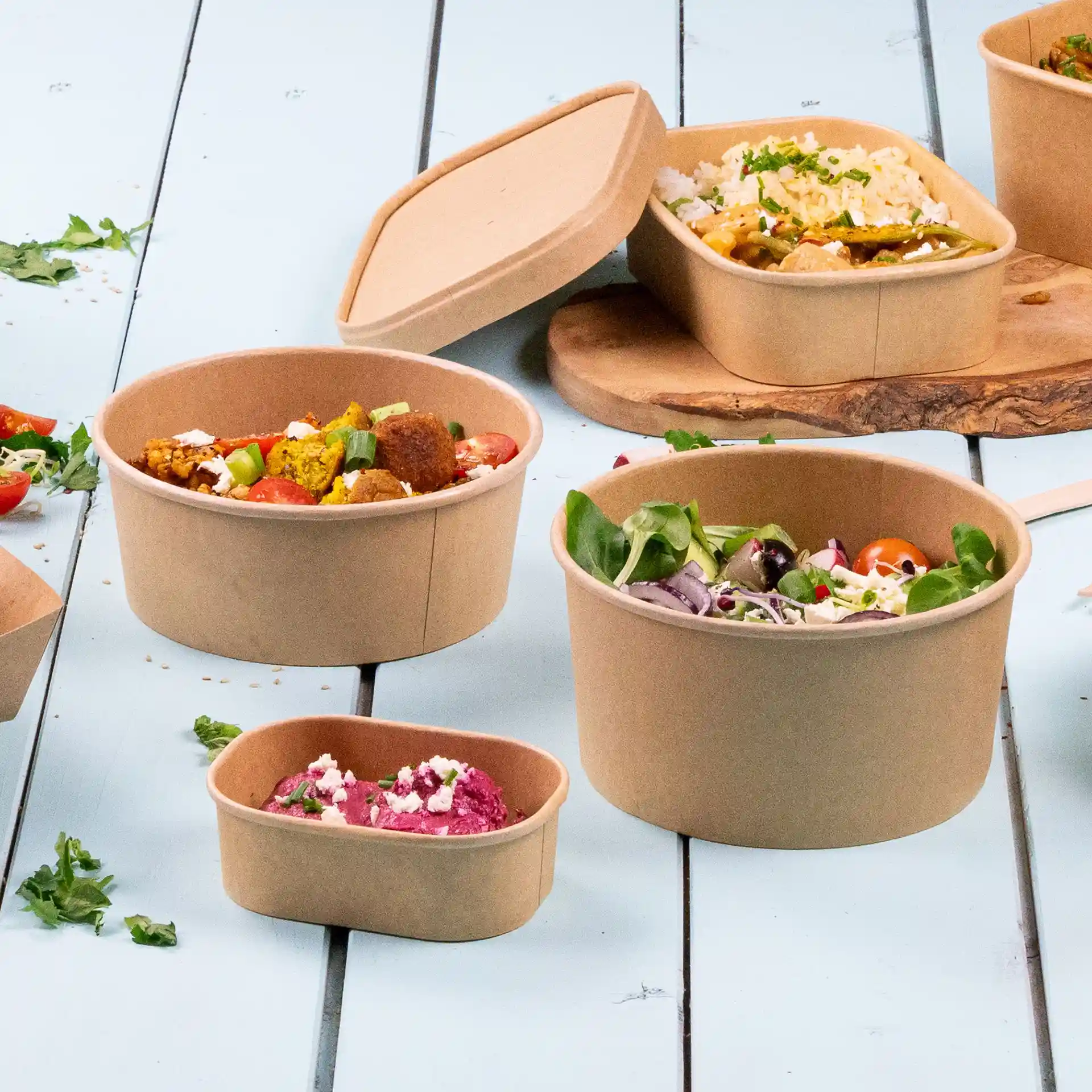 Bols en papier brun rond avec revêtement écologique, de tailles variées, remplis d'aliments sur une surface bleu clair.