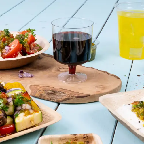 Un verre en verre transparent avec un liquide rouge est posé sur une planche en bois, entouré de bols de salade et de légumes grillés.
