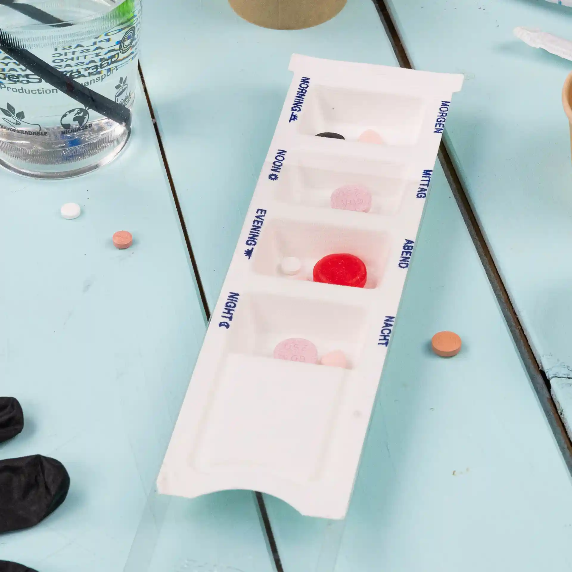 Distributeur de médicaments rectangulaire blanc avec quatre compartiments, étiquetés pour différents moments de la journée, sur une surface bleue.