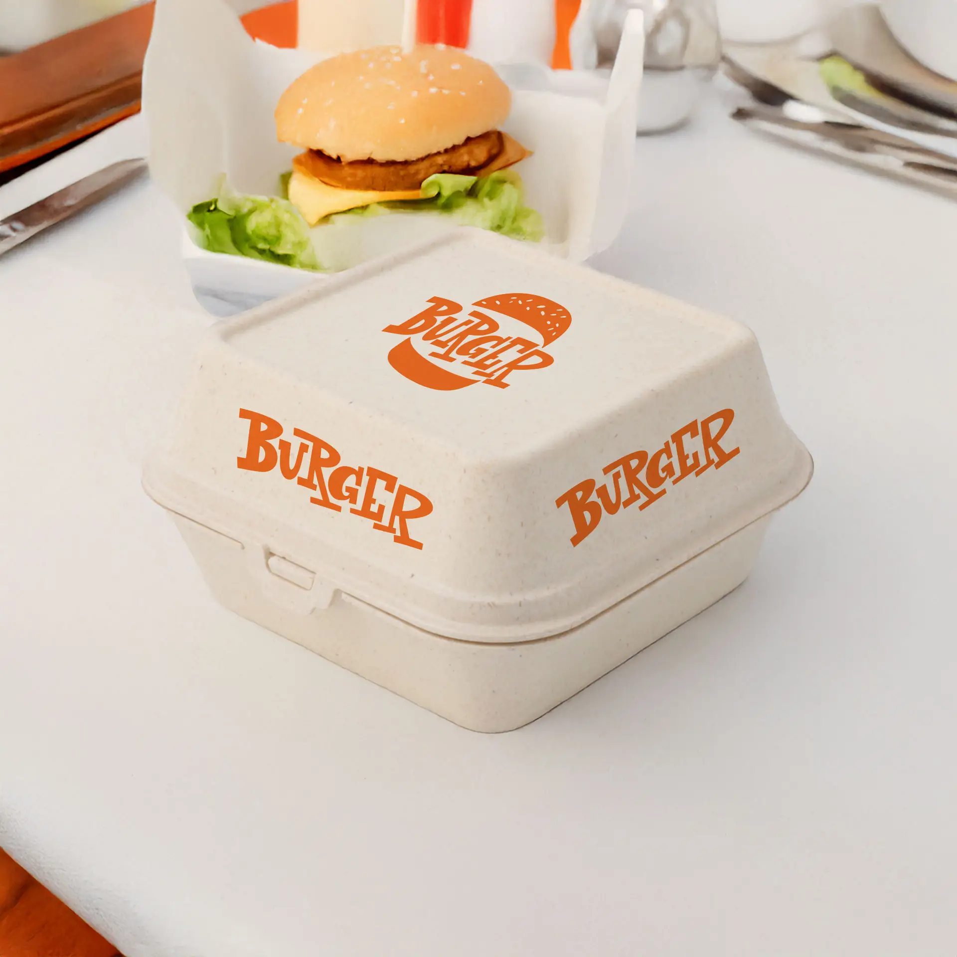 Boîte à burger réutilisable crème blanche avec logo orange "BURGER", adaptée pour aliments chauds et froids, à côté d'un hamburger sur une table.