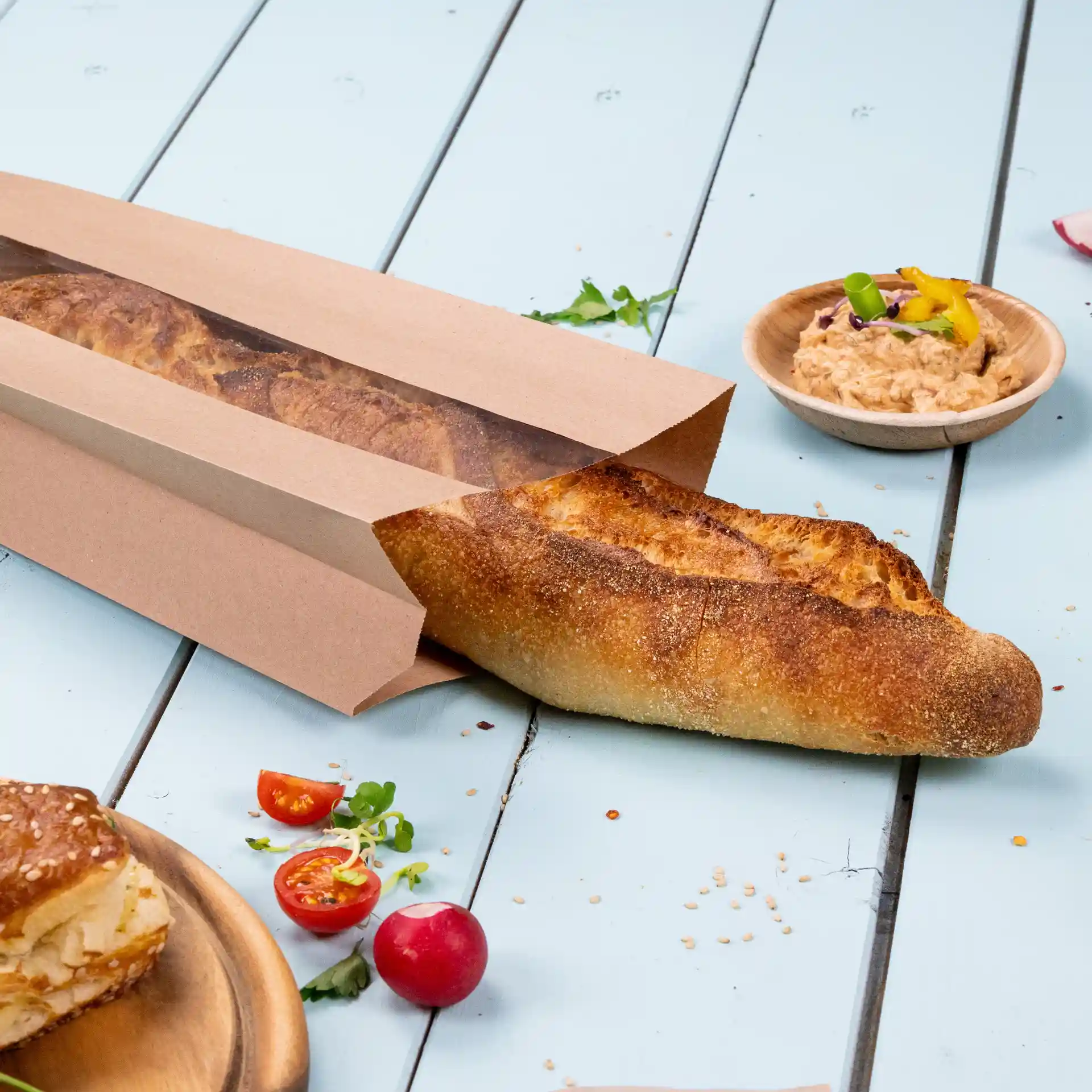 Sac à pain en papier brun plat avec une fenêtre, contenant une baguette, posé sur une surface en bois bleu clair.