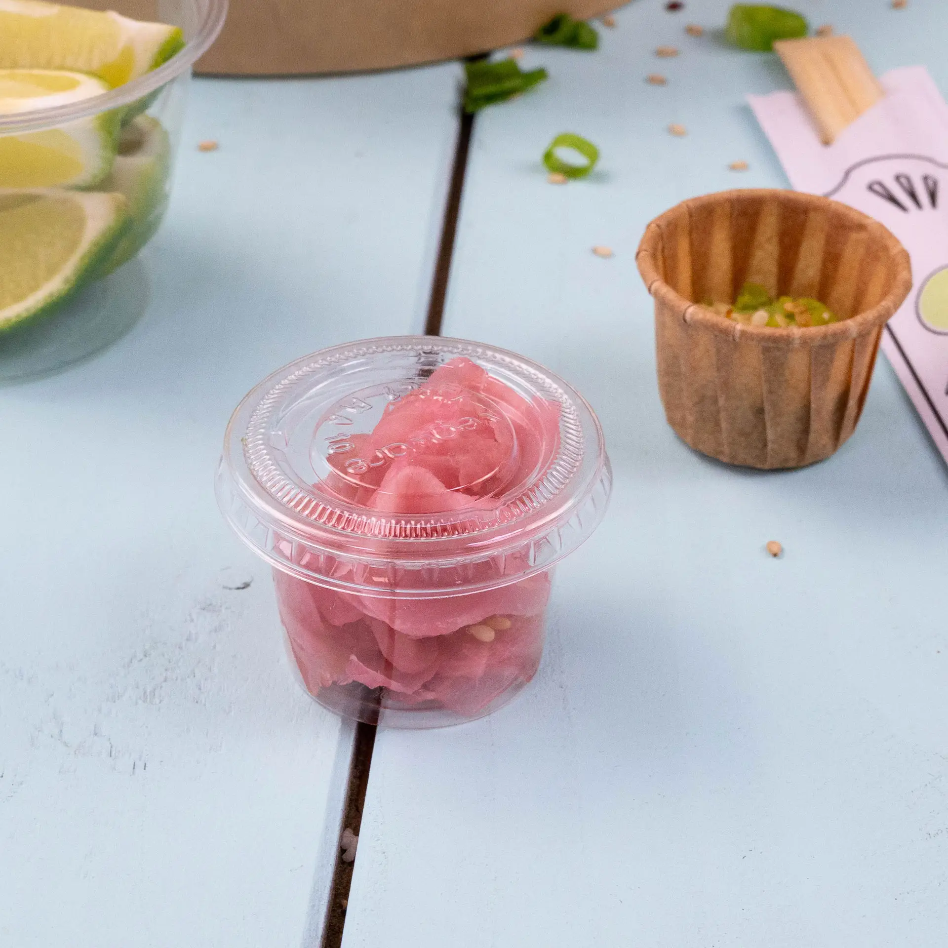 Couvercle en plastique transparent avec des légumes marinés roses à l'intérieur, posé sur une surface bleu clair.