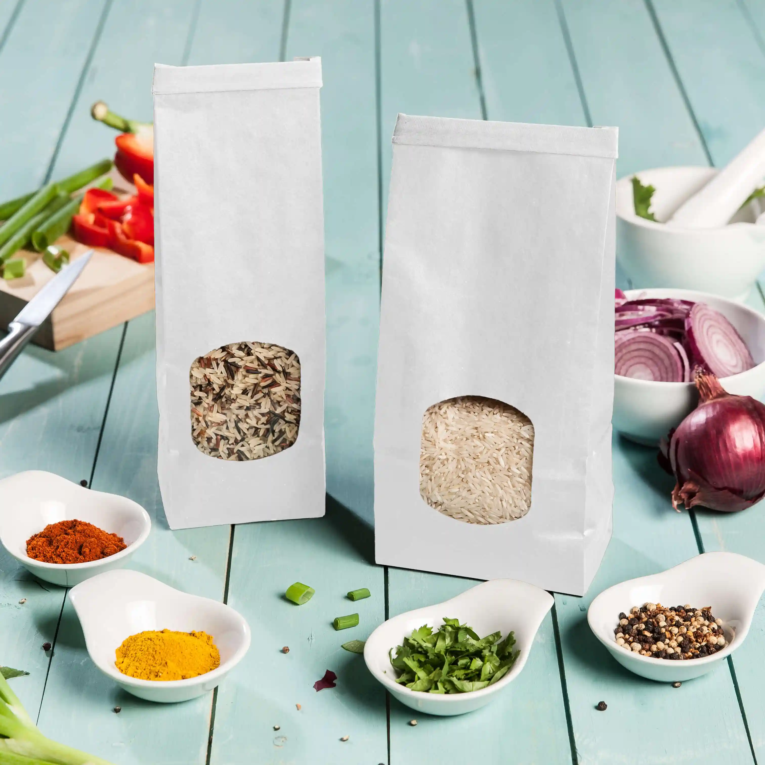 Deux sacs blancs à fond plat avec fenêtres, l'un contenant du riz mélangé et l'autre du riz blanc, sur une surface en bois bleu.