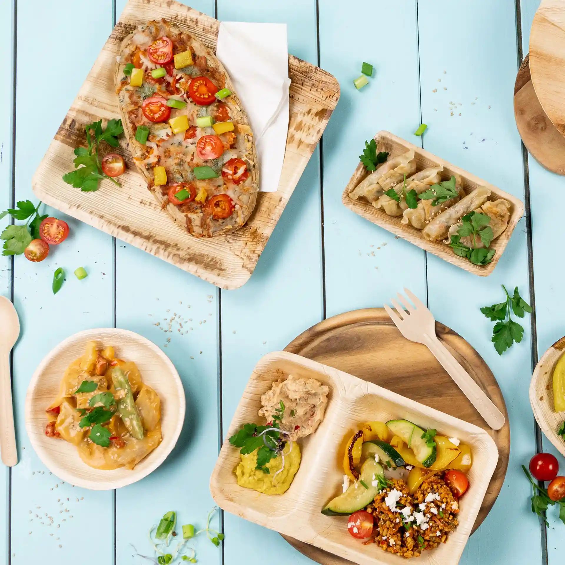 Image de divers plats servis sur des assiettes en feuilles de palmier, comprenant des légumes, des sauces et des garnitures sur une table en bois bleu.
